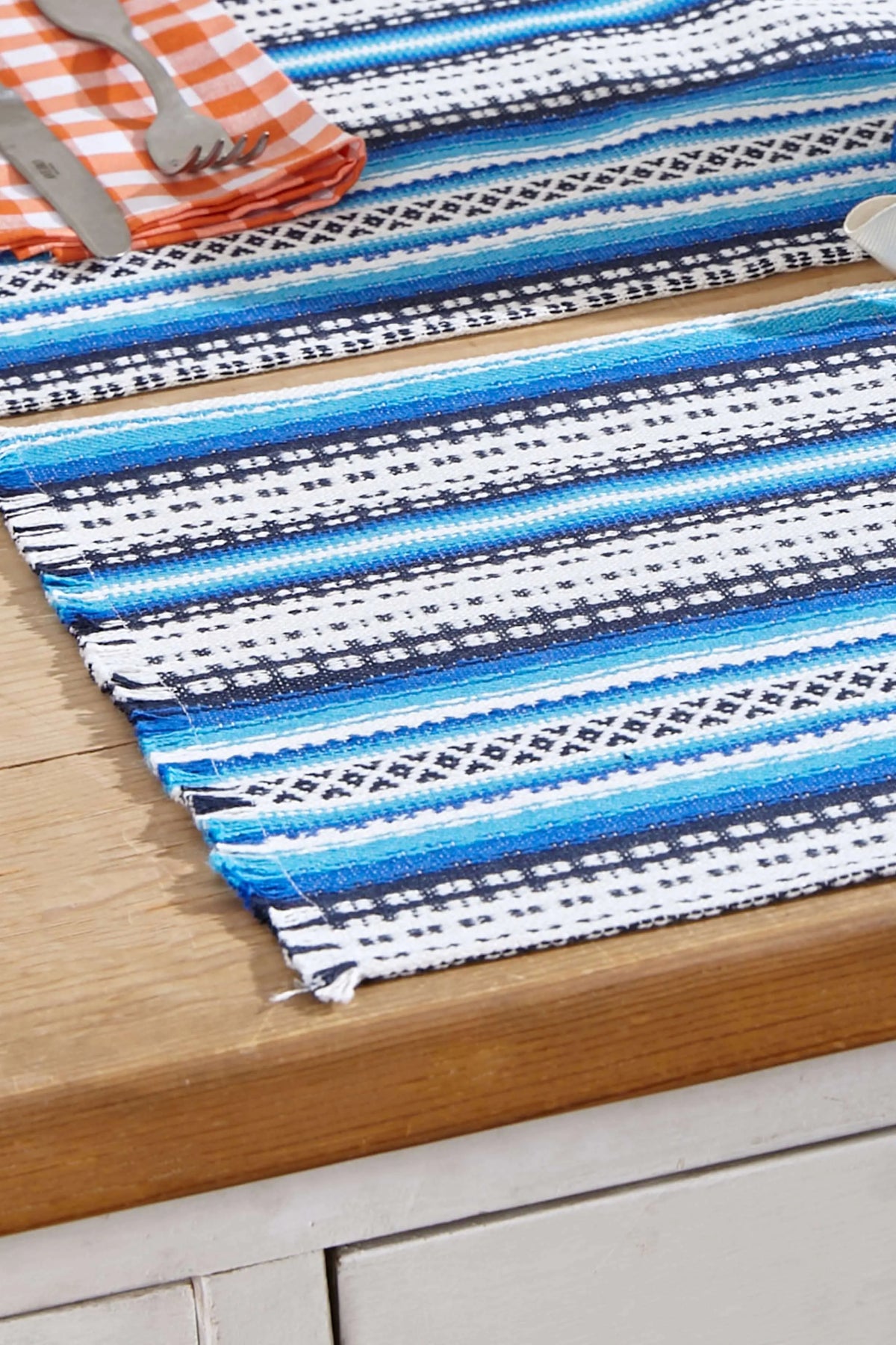 Pack de dos manteles individuales de estilo alpujarra con rayas tejidas en tonos azules y blancos sobre mesa de madera.