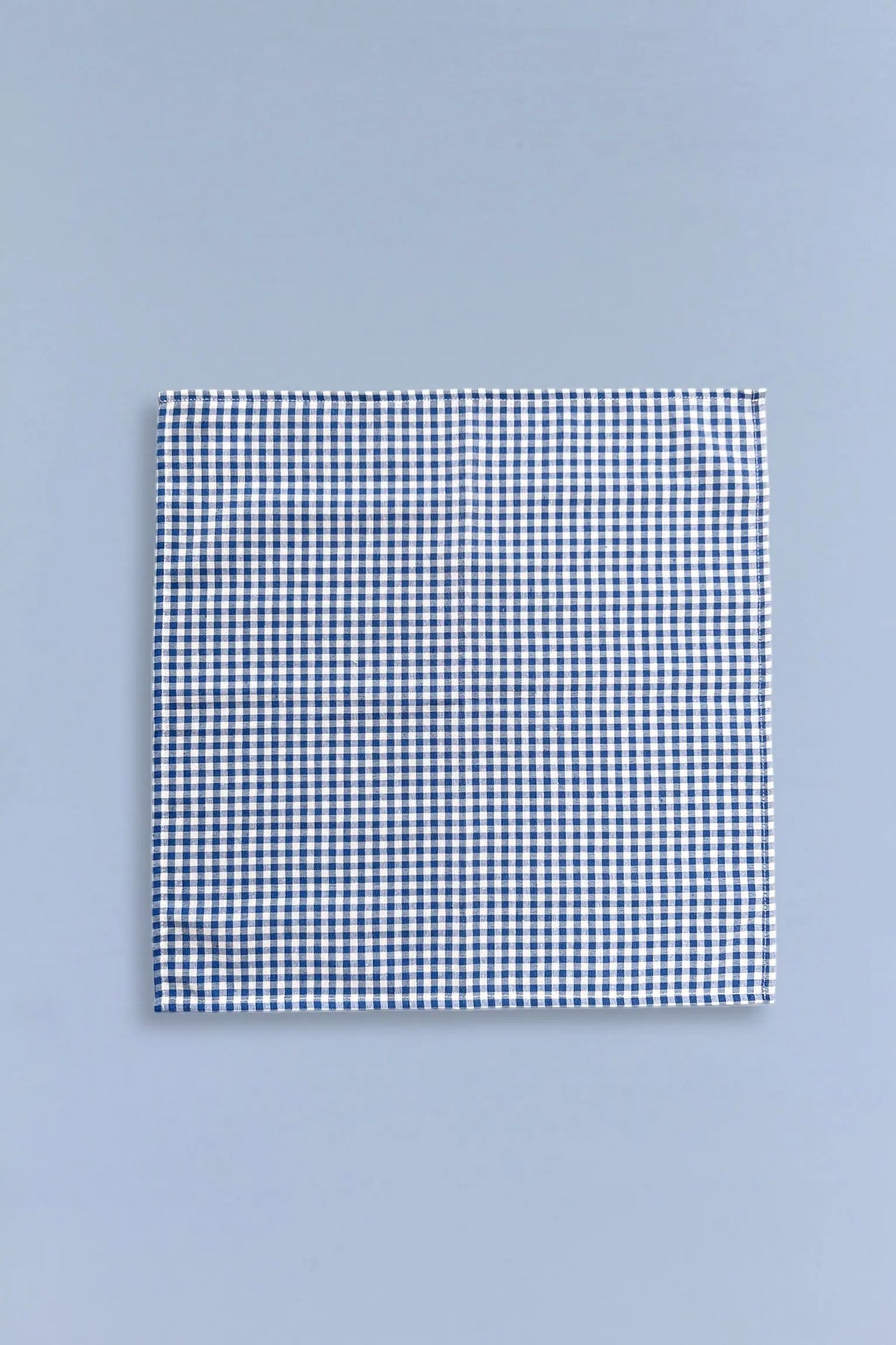 Square fabric napkin featuring a small blue and white gingham check pattern, centered on a light blue background.