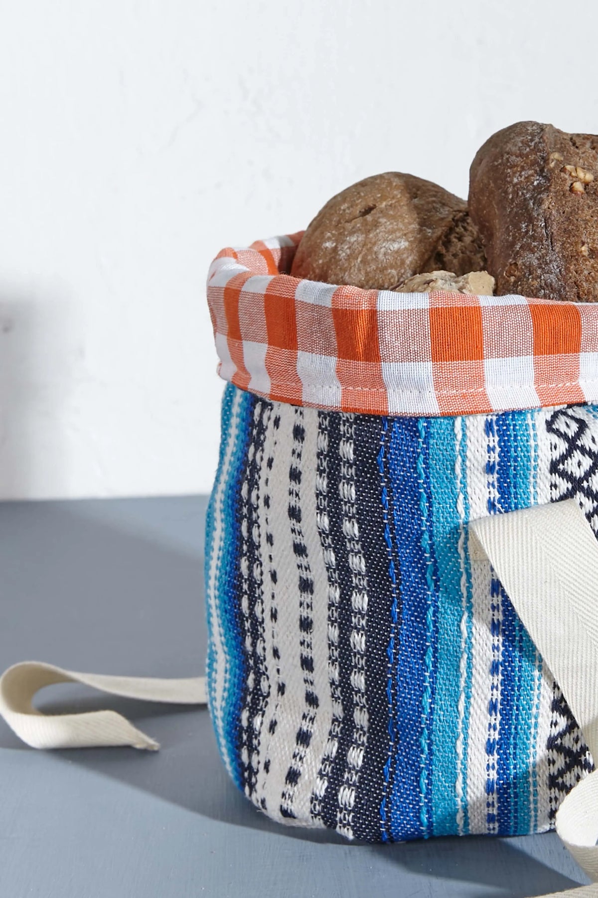 Small fabric bread basket featuring blue-toned Alpujarra stripes and an orange-and-white gingham inner lining.