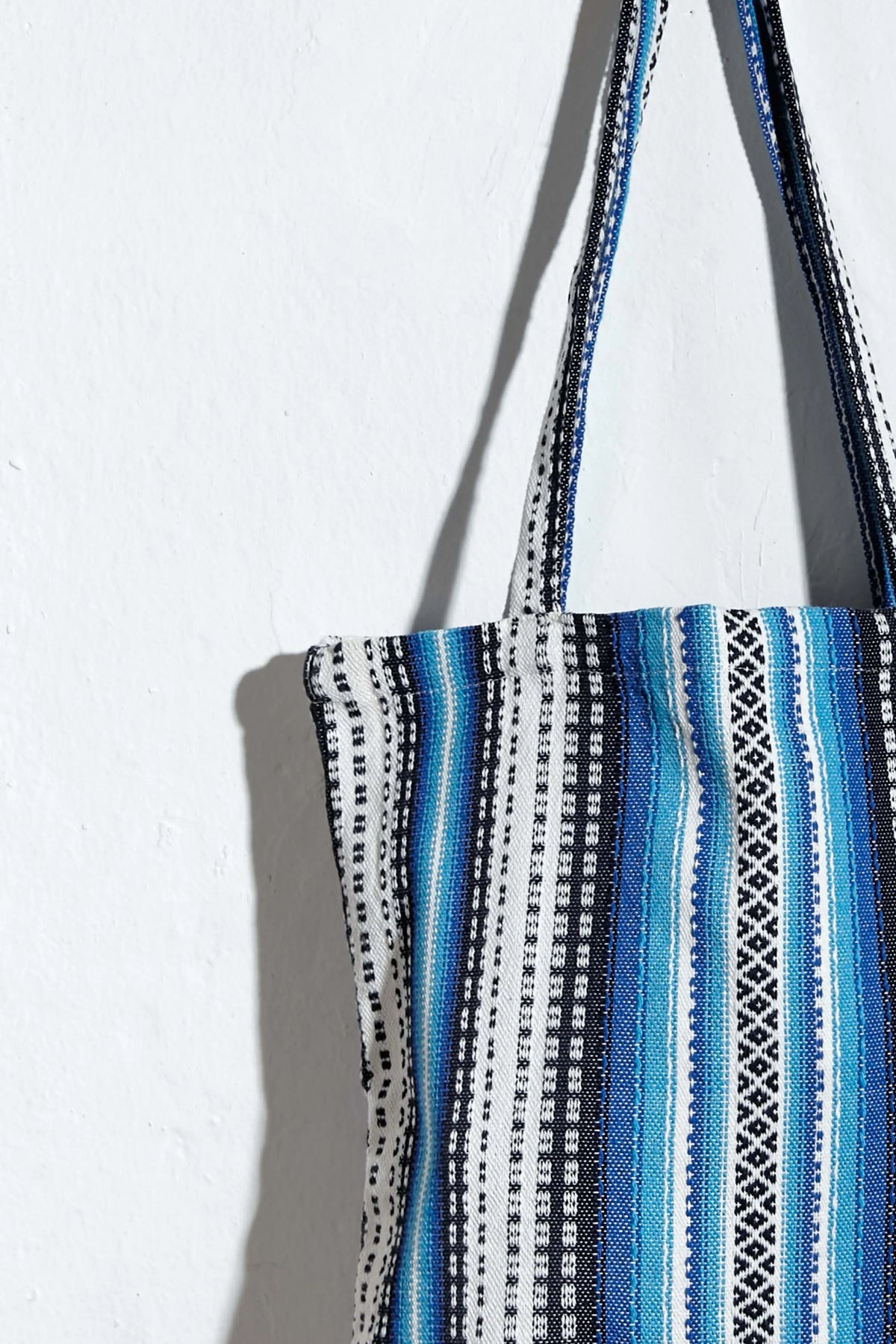 Tote bag de tela artesanal con rayas geométricas en tonos azules, blancos y negros, con diseño de estilo alpujarreño.