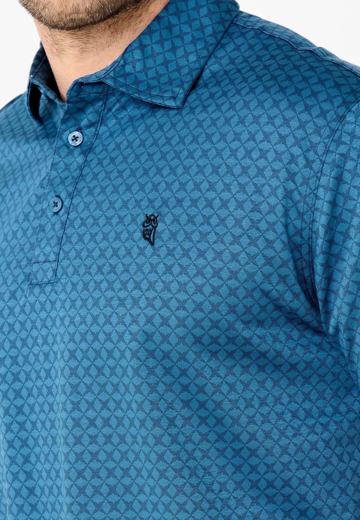 Polo azul verdoso con estampado geométrico de rombos, cuello clásico, botones y logo de búho bordado en el pecho.