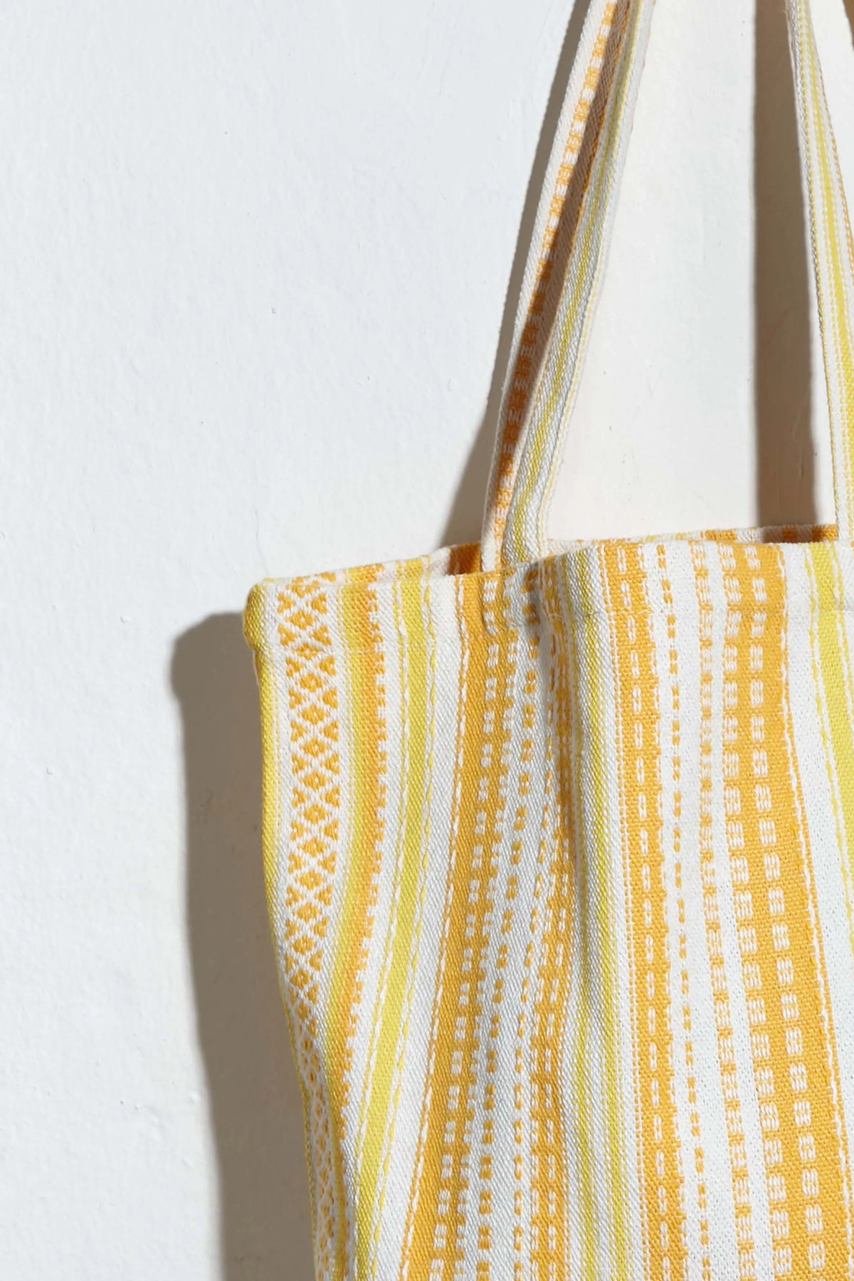 Tote bag in cream fabric with woven vertical yellow stripes and textured geometric patterns.