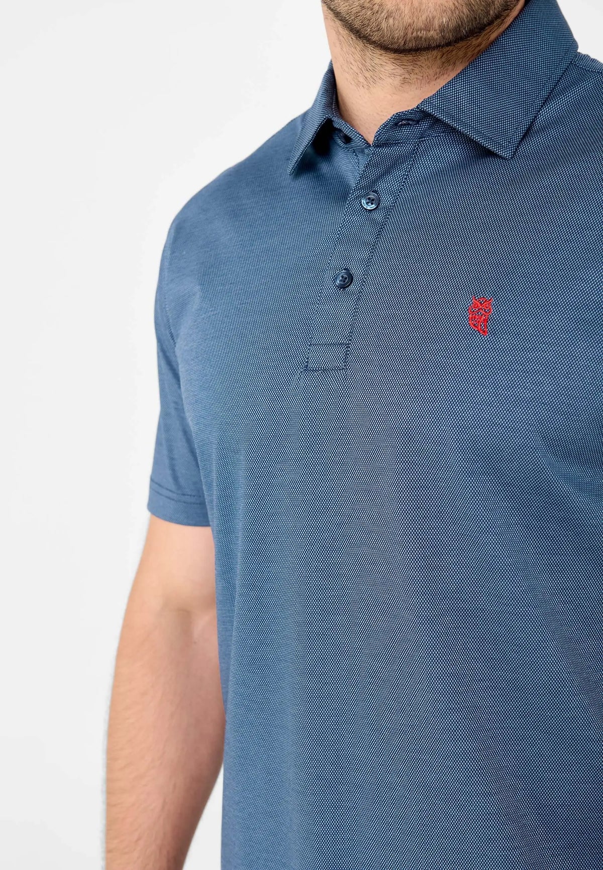 Polo azul de manga corta para hombre con tejido texturizado, cuello camisero, dos botones y logo rojo de búho.