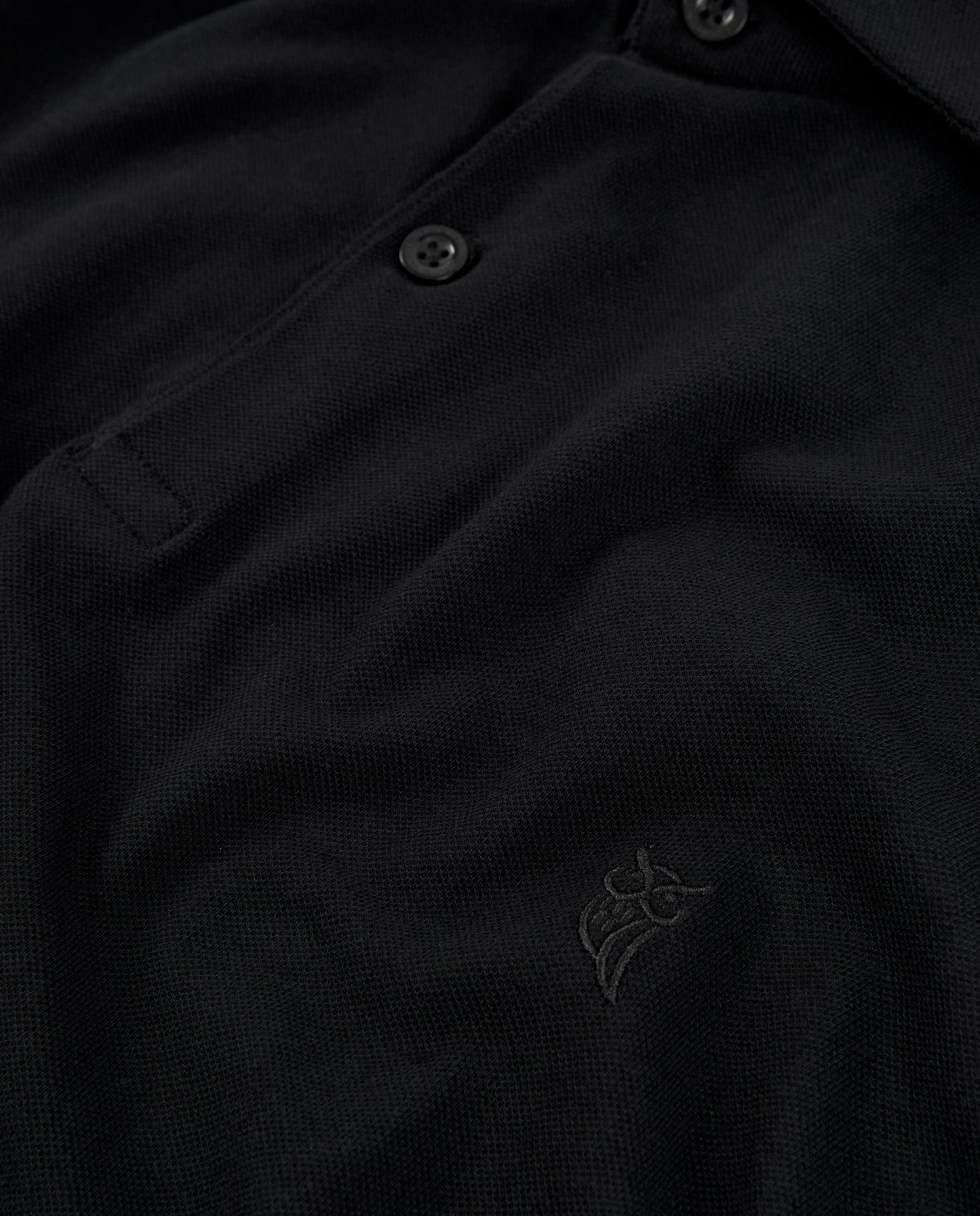 Polo negro de algodón con botones y logo bordado, estilo clásico y elegante.