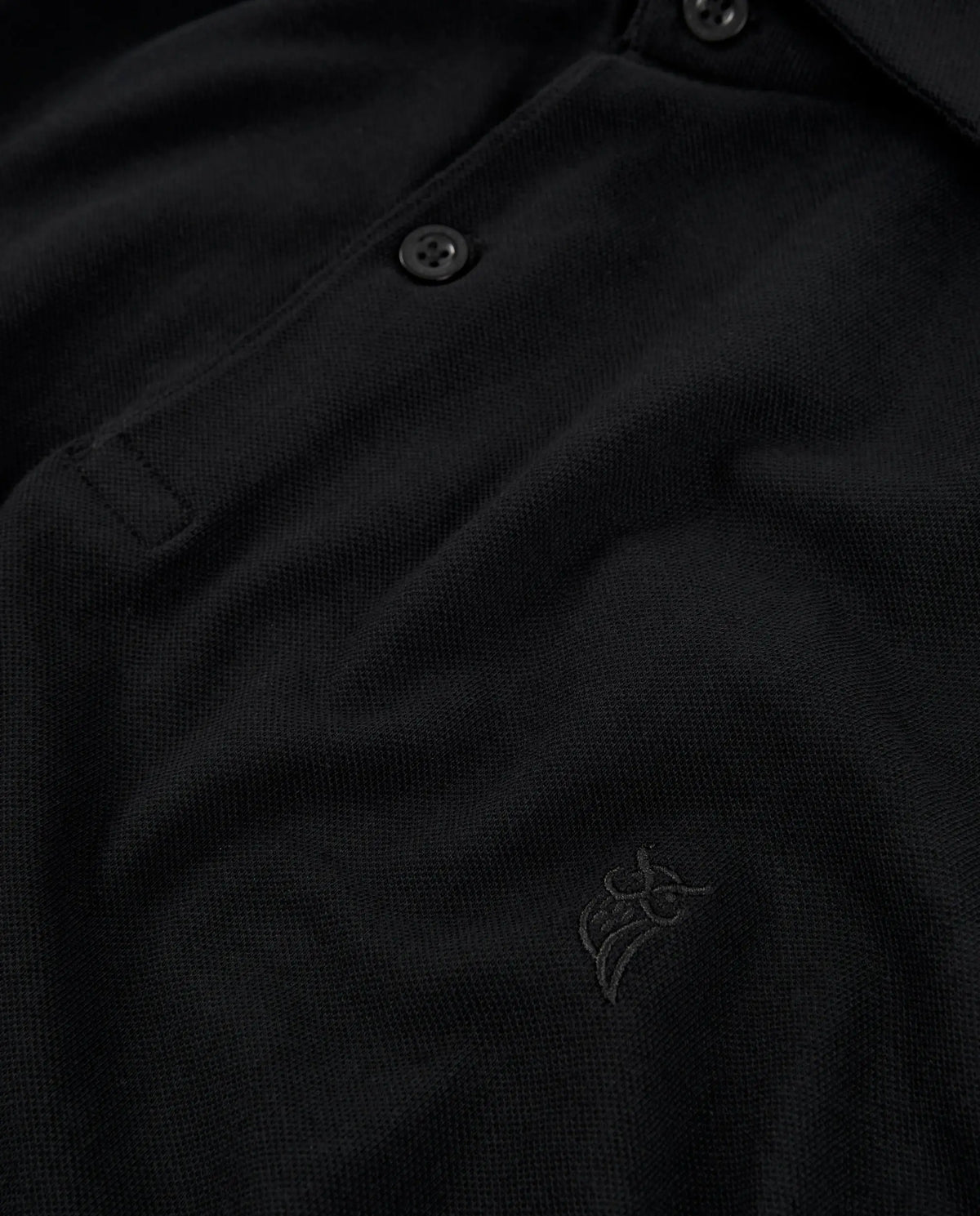 Polo negro de algodón con botones y logo bordado, estilo clásico y elegante.