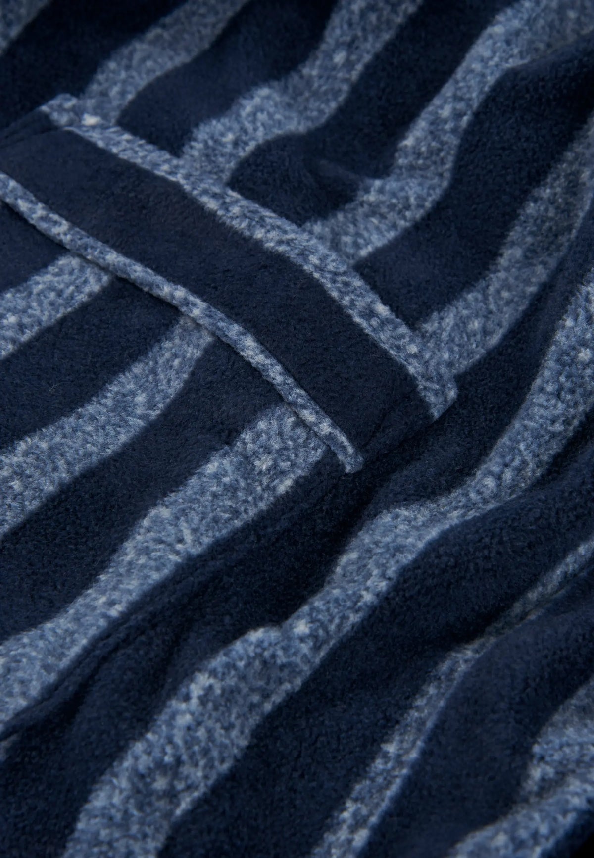 Detalle de bata de hombre en tejido polar suave con estampado de rayas anchas en tonos azul marino y azul jaspeado.