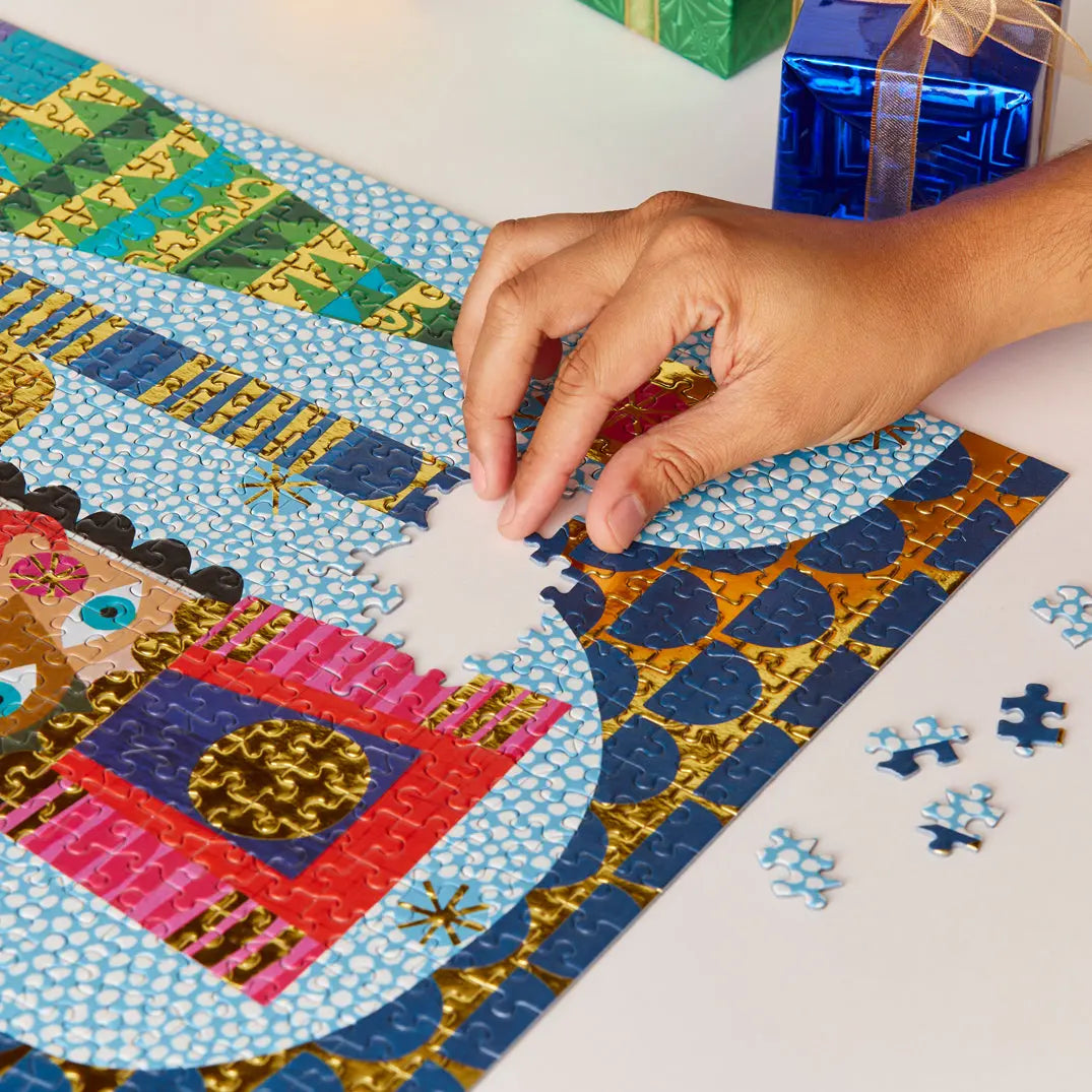 Hand placing piece in a festive 1000-piece jigsaw puzzle featuring a Nutcracker design with vibrant gold foil accents.