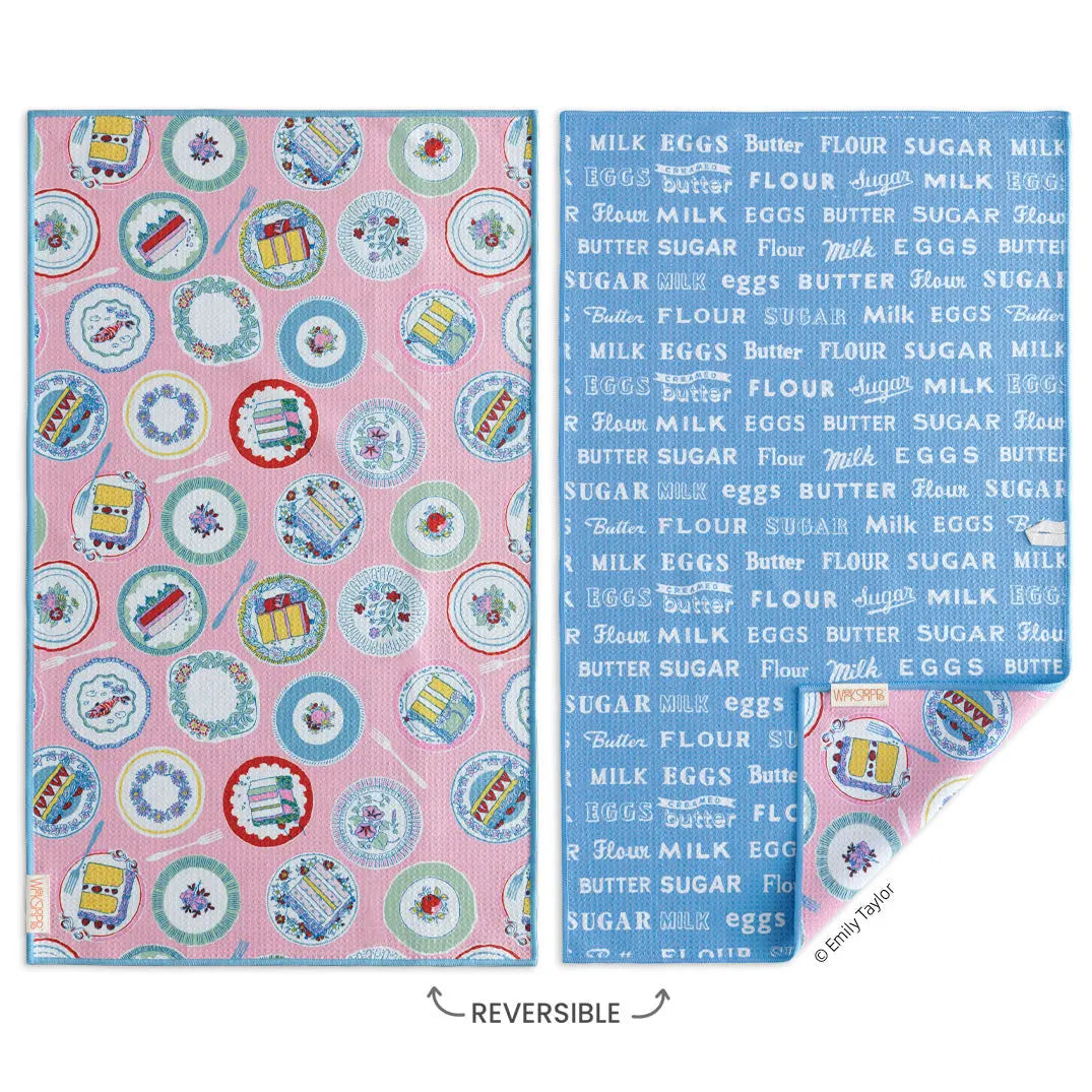 Reversible microfiber towel with pink cake and dish pattern on one side, and blue baking ingredient text on the other.
