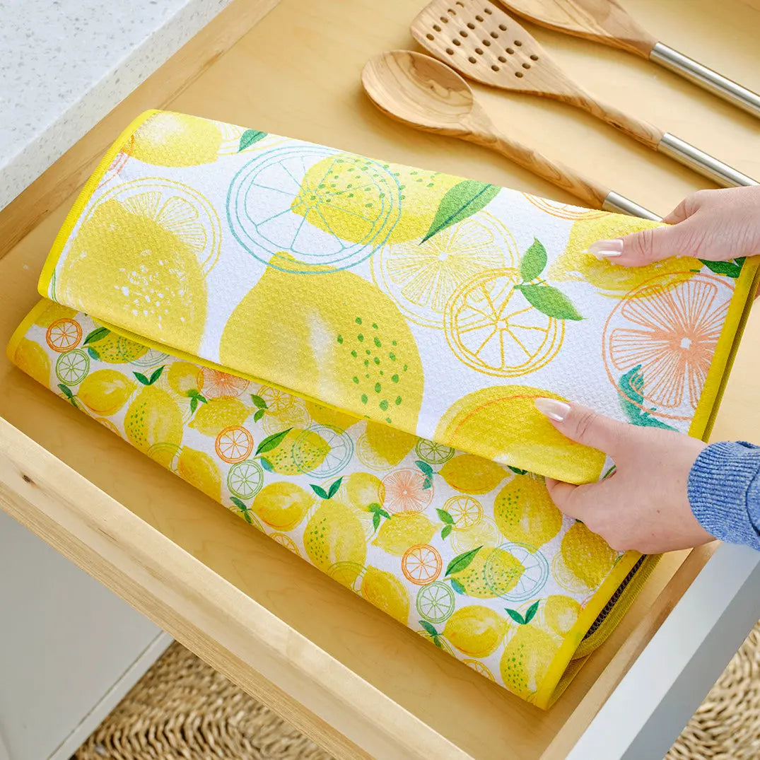 Soft, foldable dish drying mat with a white background featuring vibrant yellow lemons, green leaves, and orange slices.