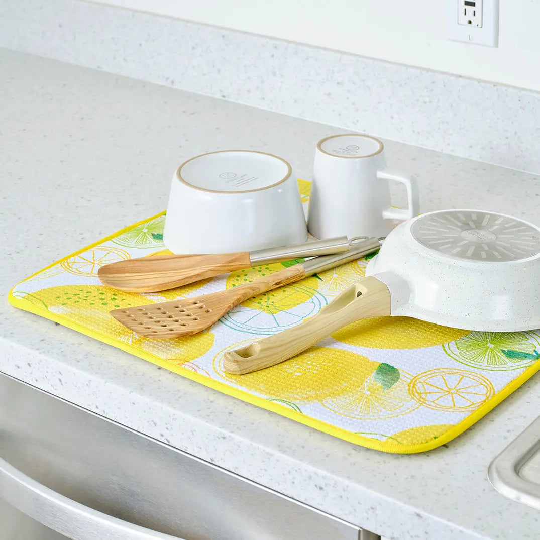 Lemon-patterned dish drying mat in yellow, white, and green holding kitchenware on a speckled countertop.