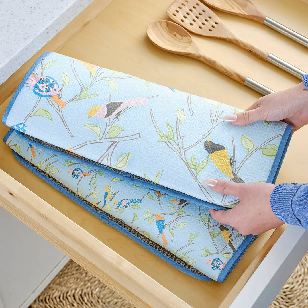 Light blue absorbent dish drying mat with a whimsical bird and branch pattern, featuring a mesh texture and blue trim.