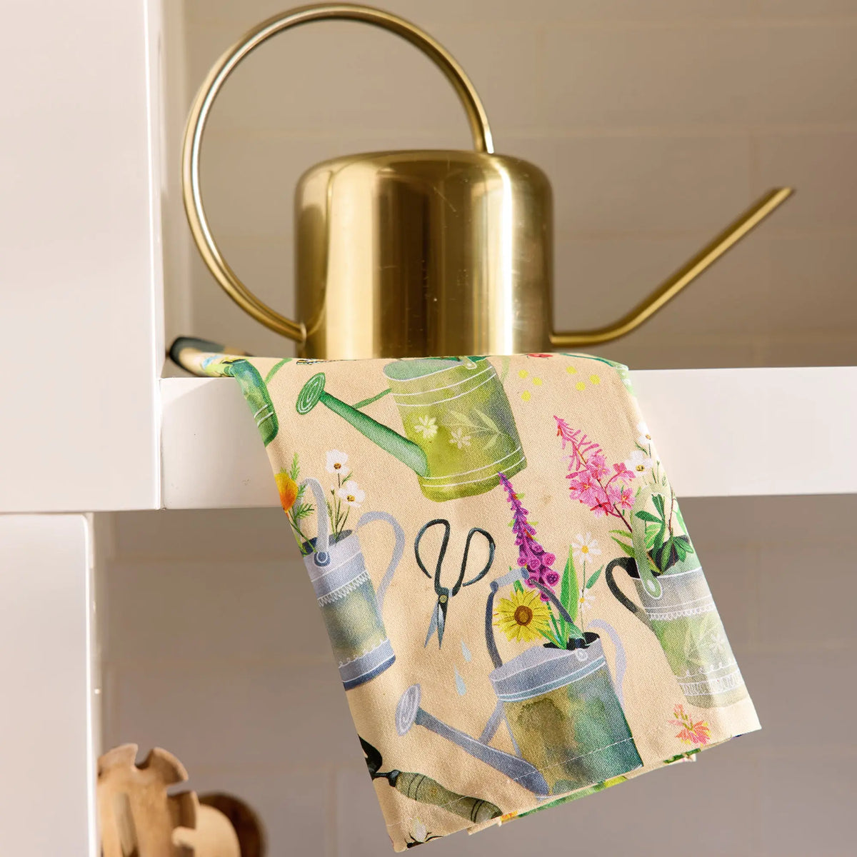 Cotton tea towel featuring watercolor-style illustrations of garden tools and flowers on a light beige background.