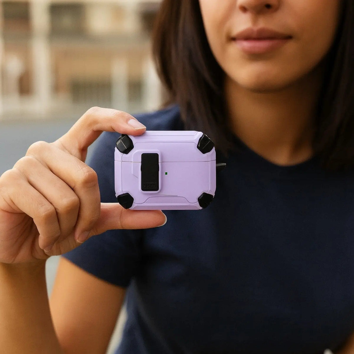 Person holding a rugged, light purple AirPods Pro case with black corner bumpers and a secure black locking latch.