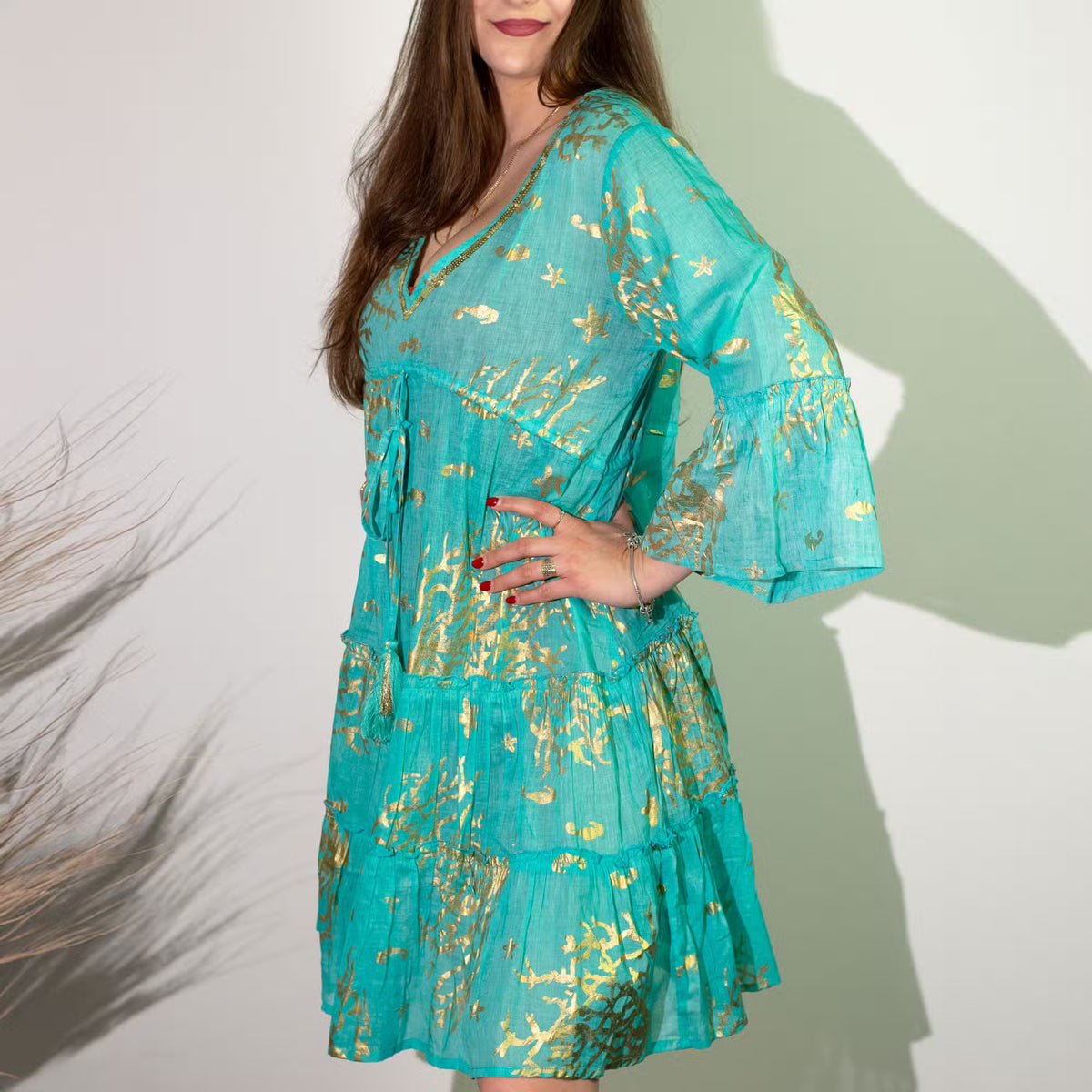 Vestido corto turquesa con estampado de corales dorados, cuello en V, mangas acampanadas y corte escalonado.