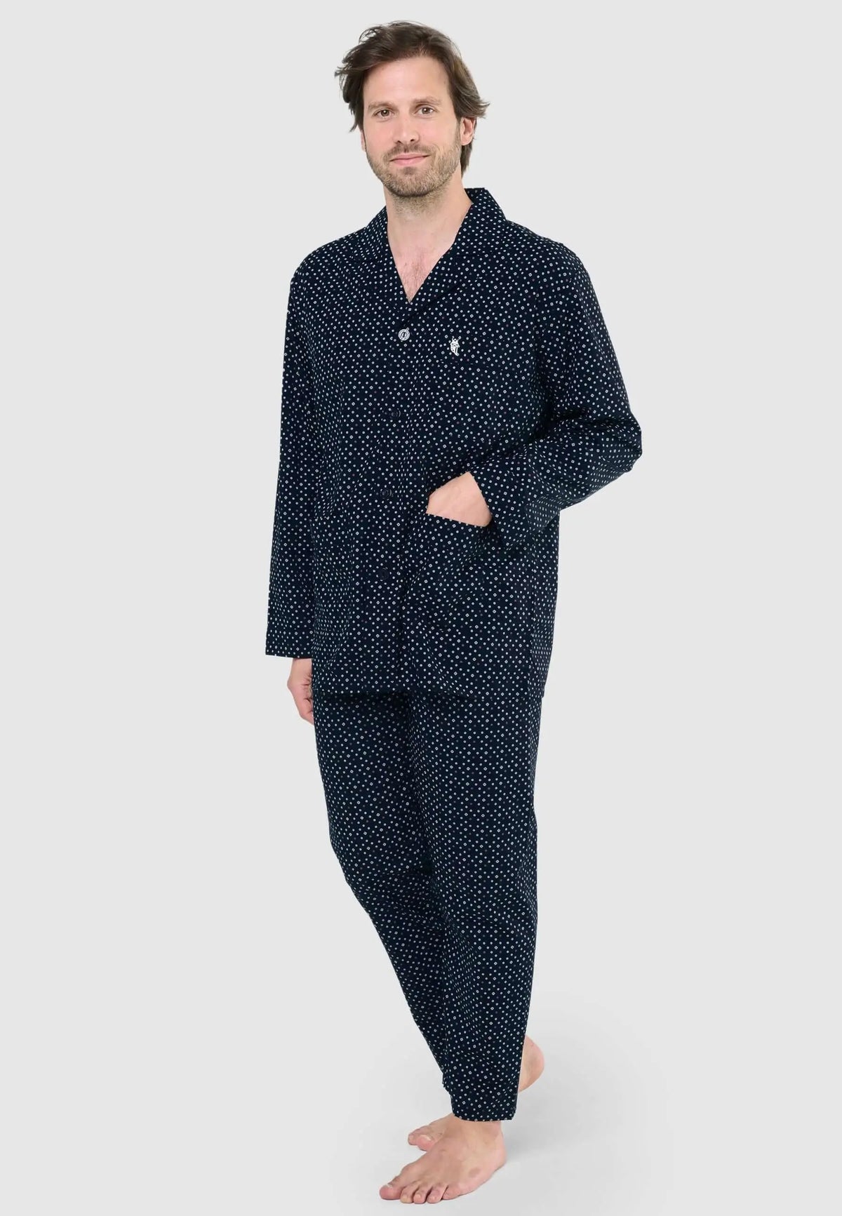 Hombre vistiendo pijama largo azul marino con estampado de pequeños puntos blancos, cuello solapa y botones delanteros.
