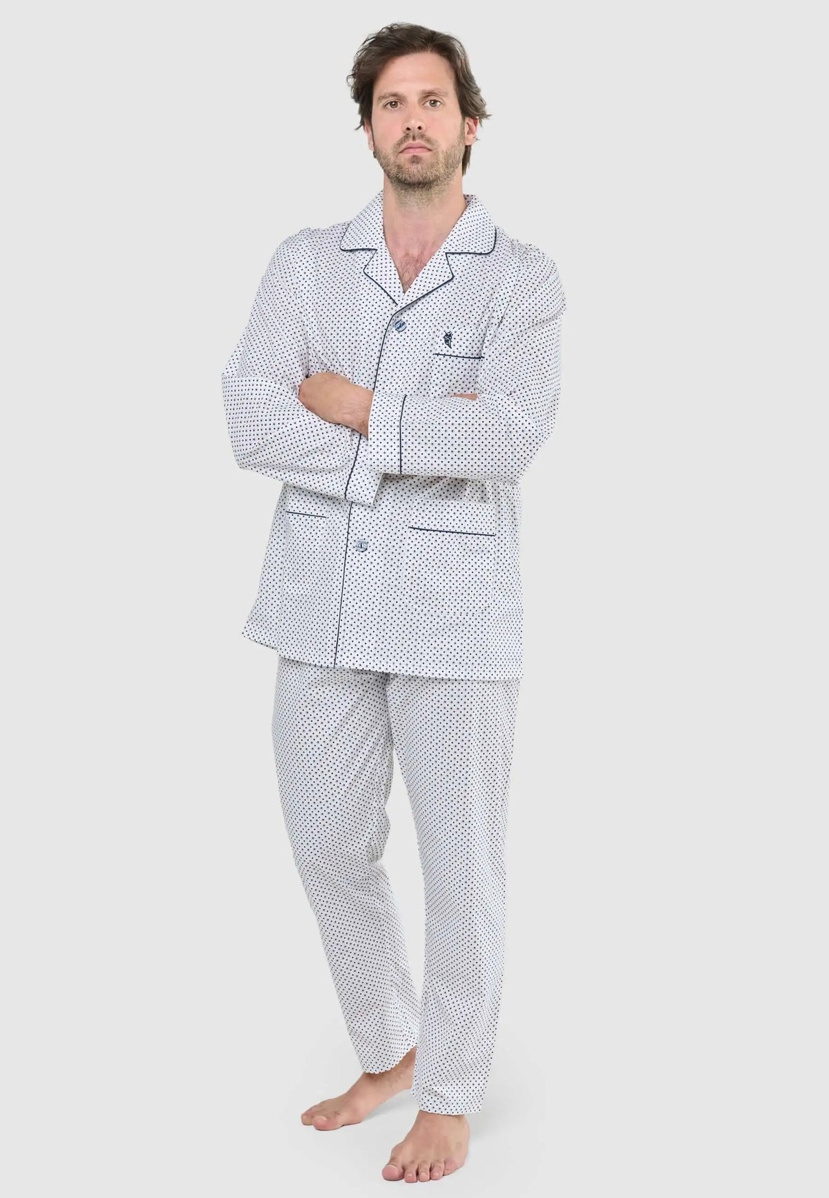 Hombre con pijama largo de botones, estampado de puntos azules sobre fondo blanco, cuello solapa y ribetes oscuros.