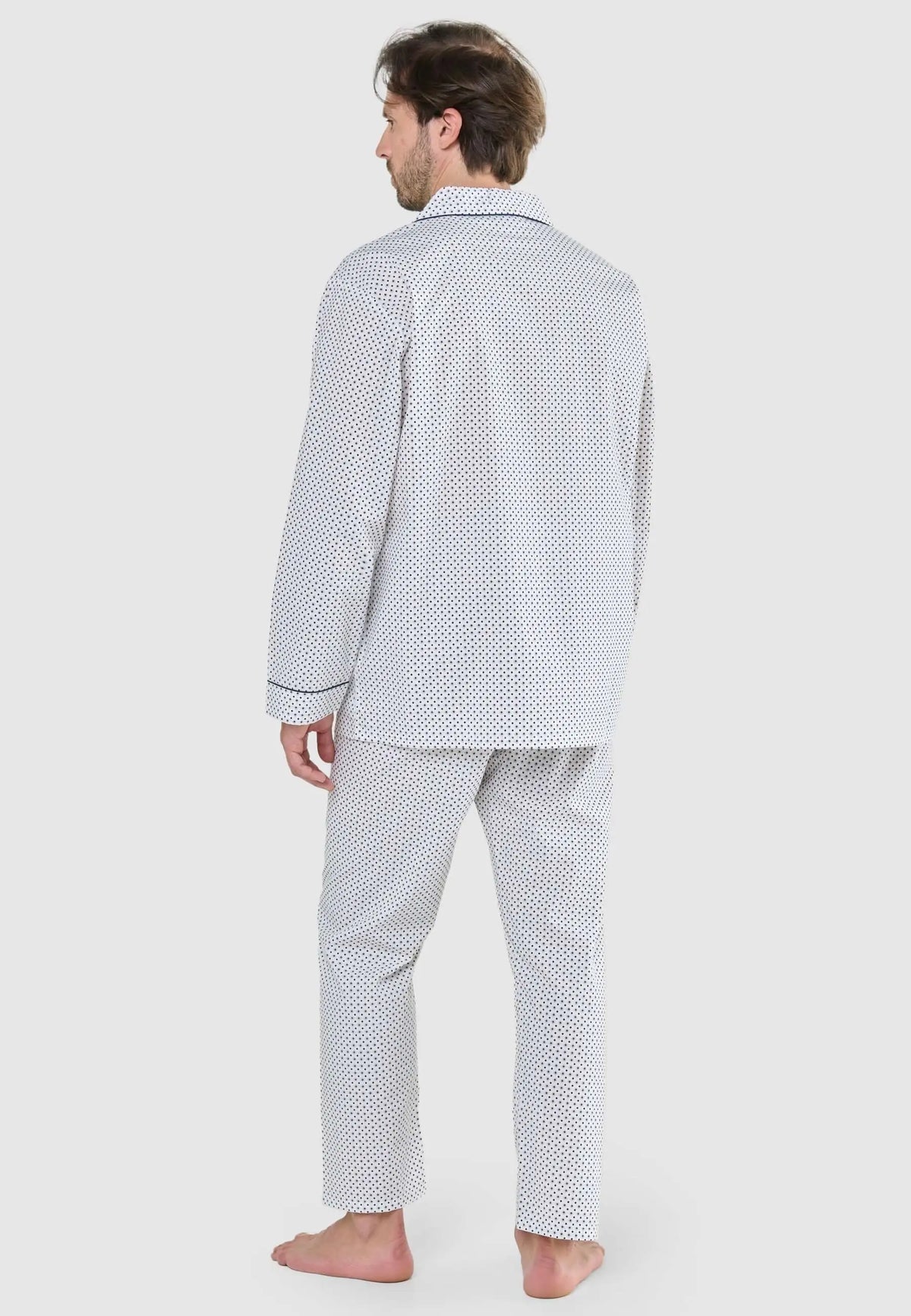 Hombre de espaldas con pijama largo de camisa con solapa y pantalón, estampado de pequeños puntos azules sobre blanco.