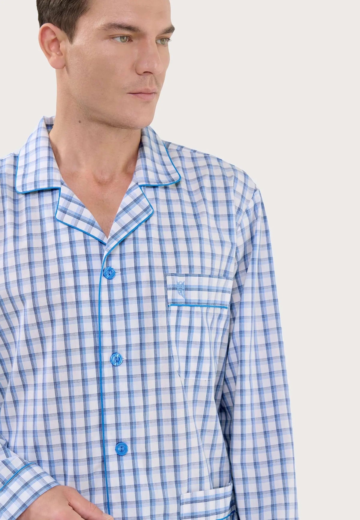 Pijama hombre de cuadros azul y blanco con solapa, cierre de botones y bolsillo con bordado, puesto por un modelo.