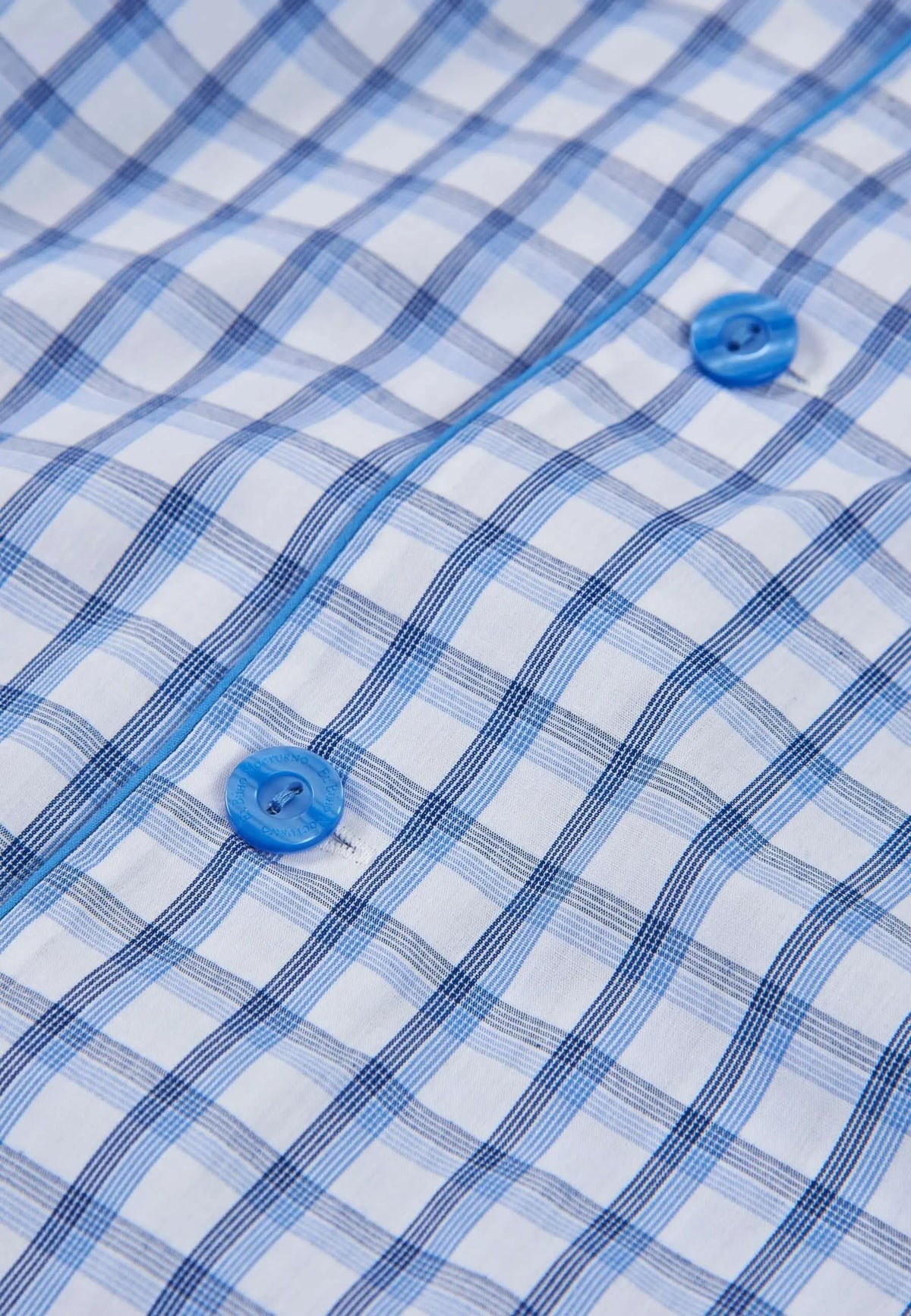 Detalle de pijama de hombre con estampado de cuadros azules y blancos, tejido fino y botones azules.