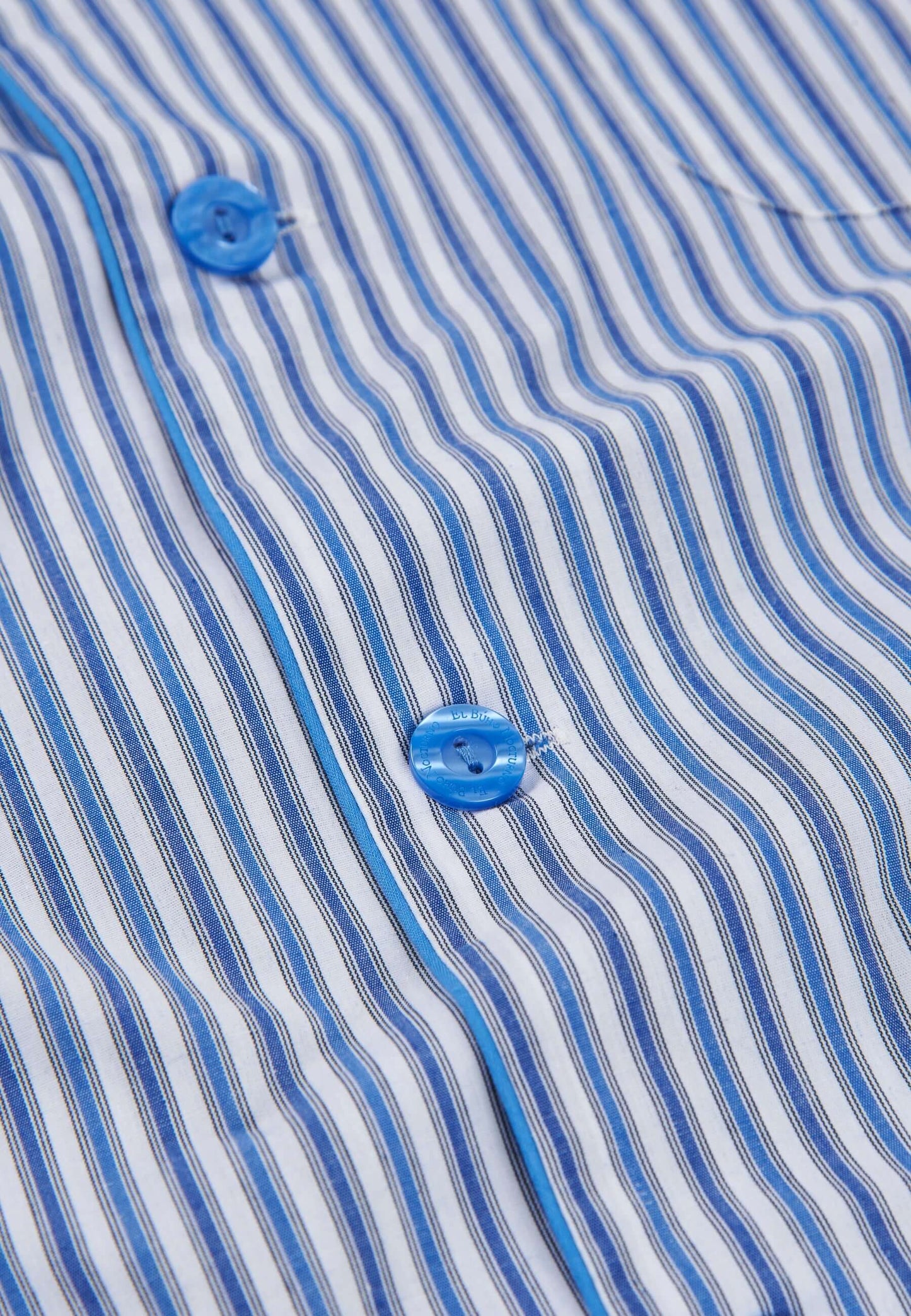 Detalle de pijama de hombre de popelín con rayas azules y blancas, botones azules y vivo decorativo a juego.