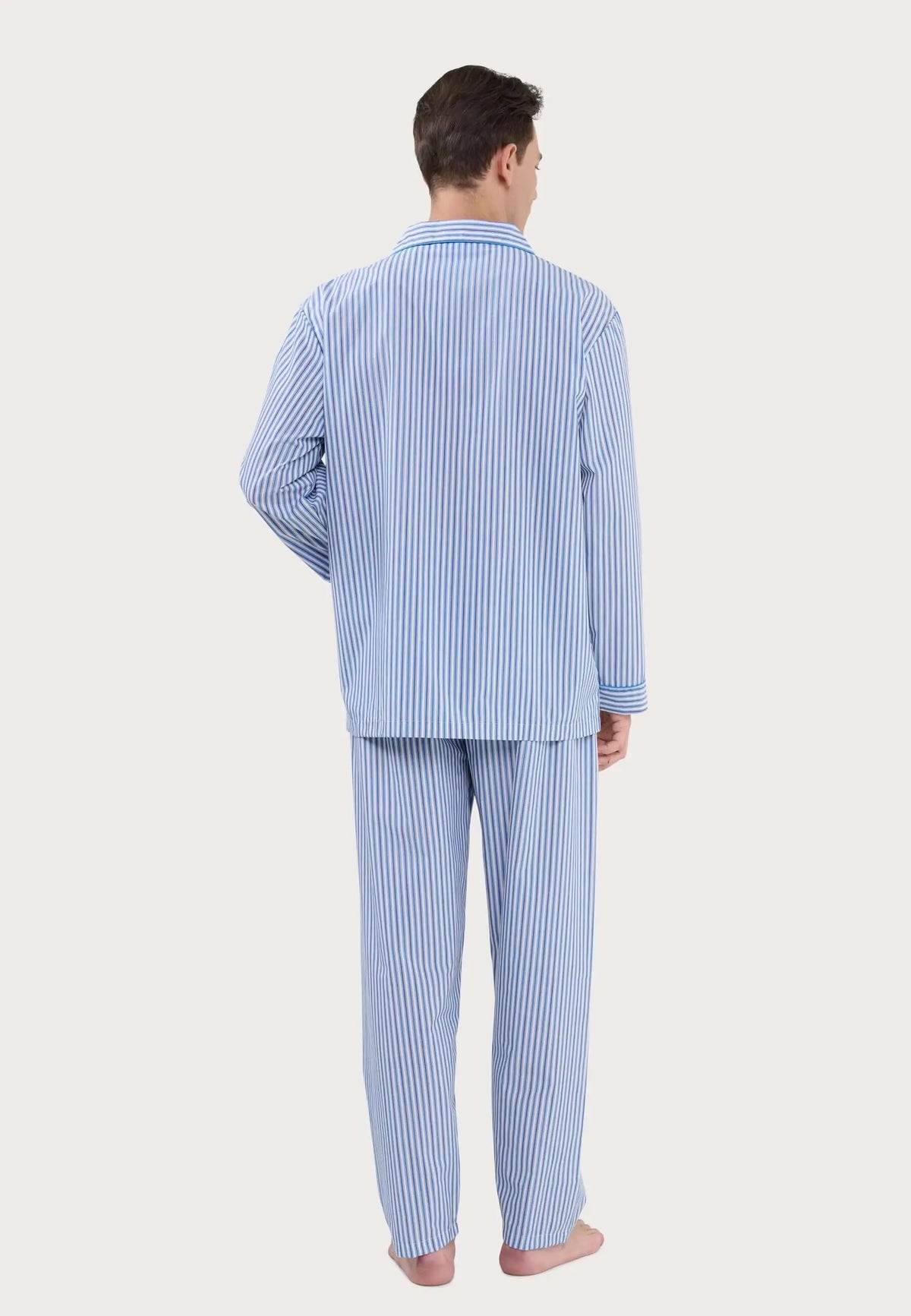 Hombre de espaldas vistiendo pijama largo de algodón azul con rayas verticales blancas, cuello solapa y ajuste cómodo.