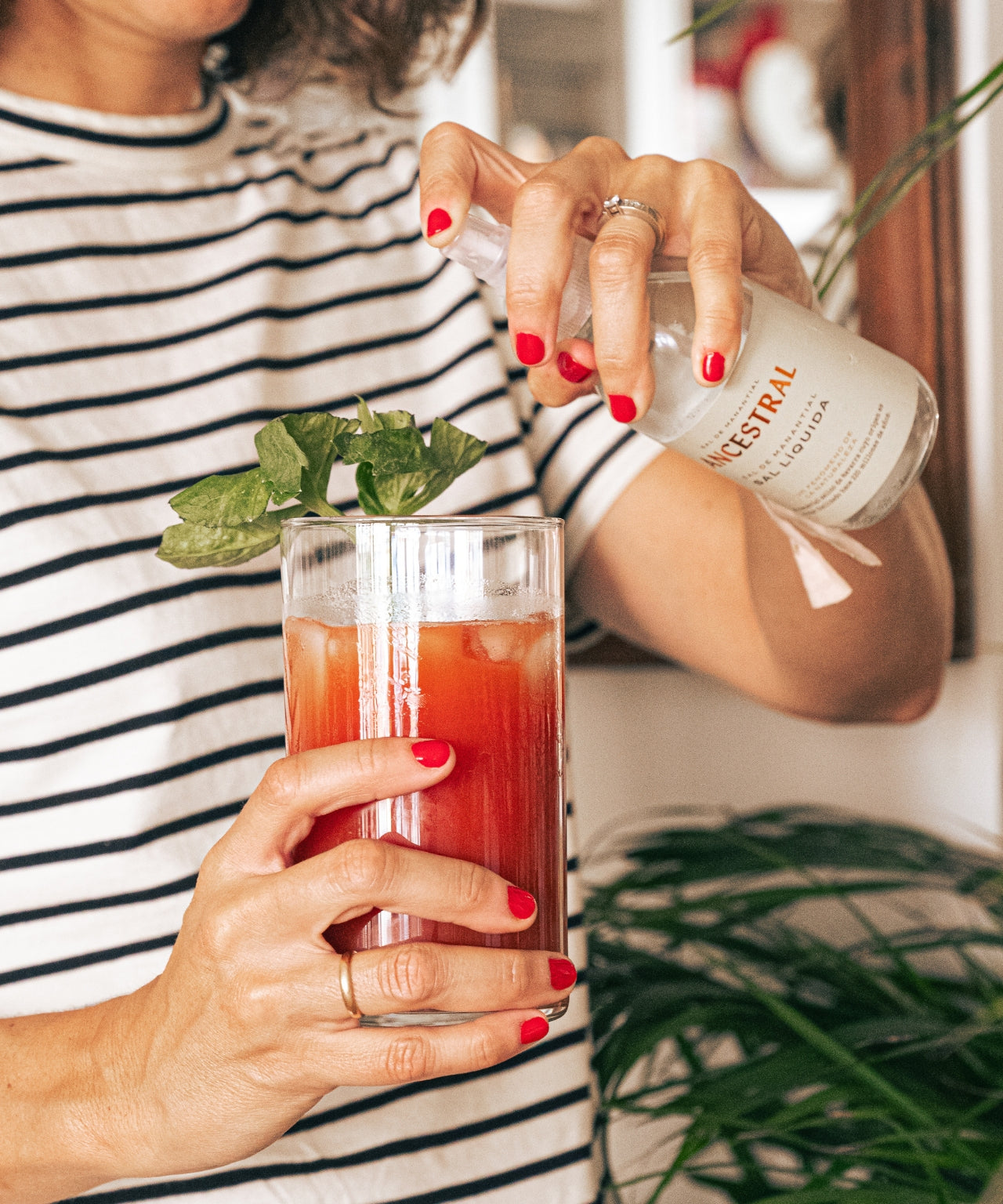 Person in striped shirt sprays liquid salt from a 200ml clear bottle into a glass of red drink with mint garnish.