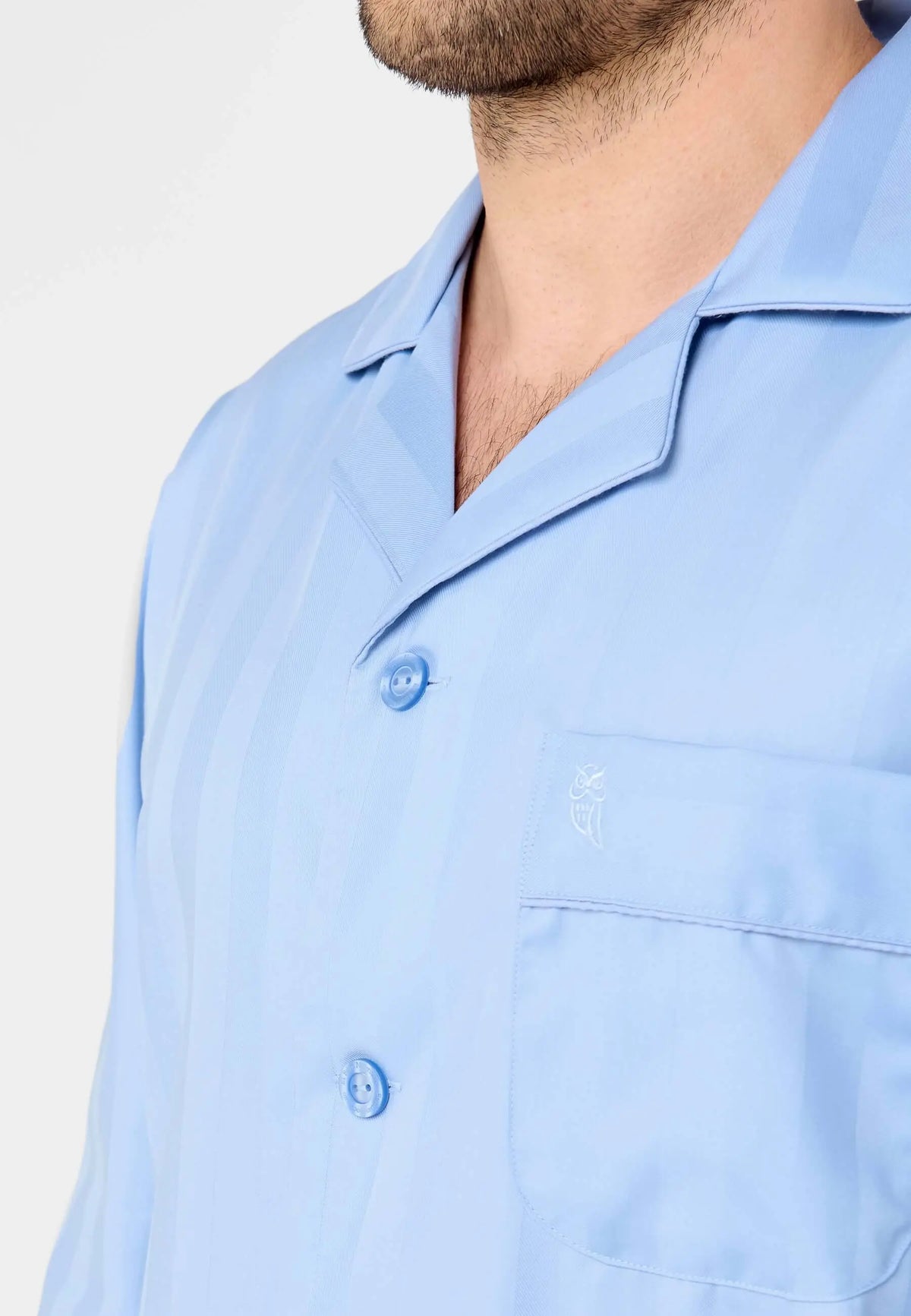 Pijama hombre azul claro, tejido con rayas verticales, cuello solapa, botones a tono y logo bordado en bolsillo frontal.