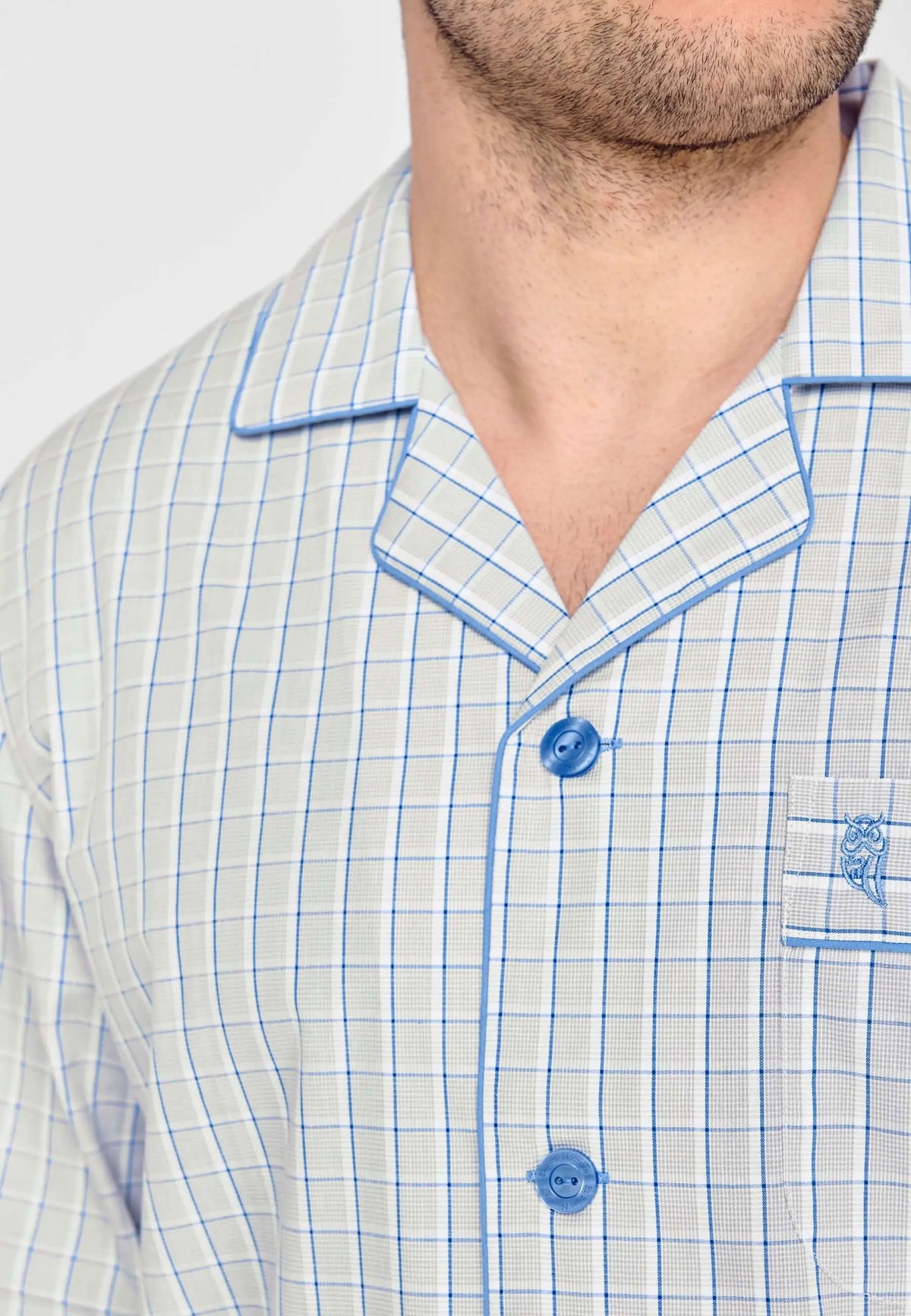Pijama de hombre gris a cuadros azules con solapas, bolsillo con logo de búho bordado y botones azules en el pecho.