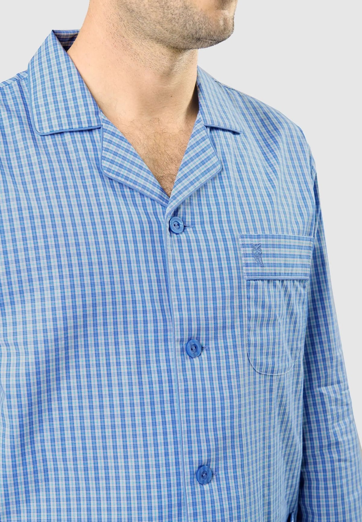 Pijama de hombre azul con estampado de cuadros, cuello de solapa, botones frontales y bolsillo con logo bordado.