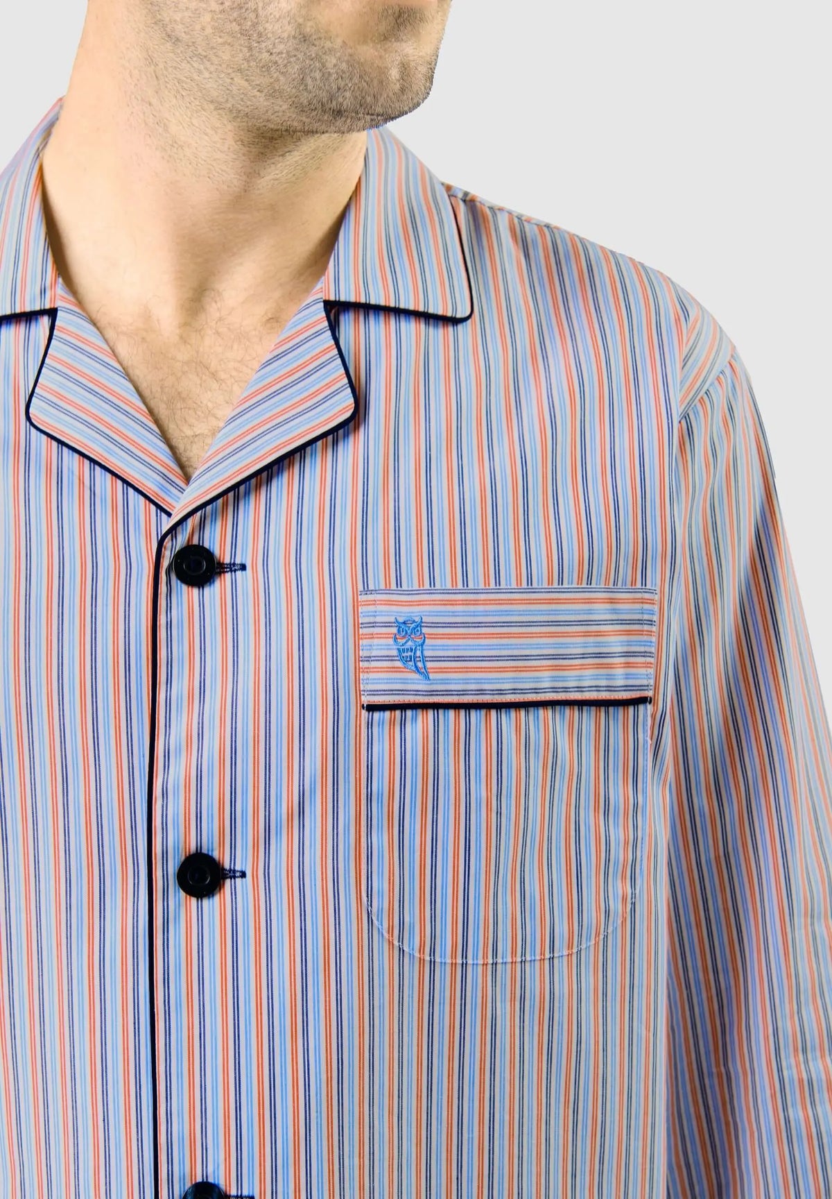 Pijama de hombre a rayas naranja y azul con cuello solapa, botones oscuros, bolsillo frontal y logo de búho bordado.