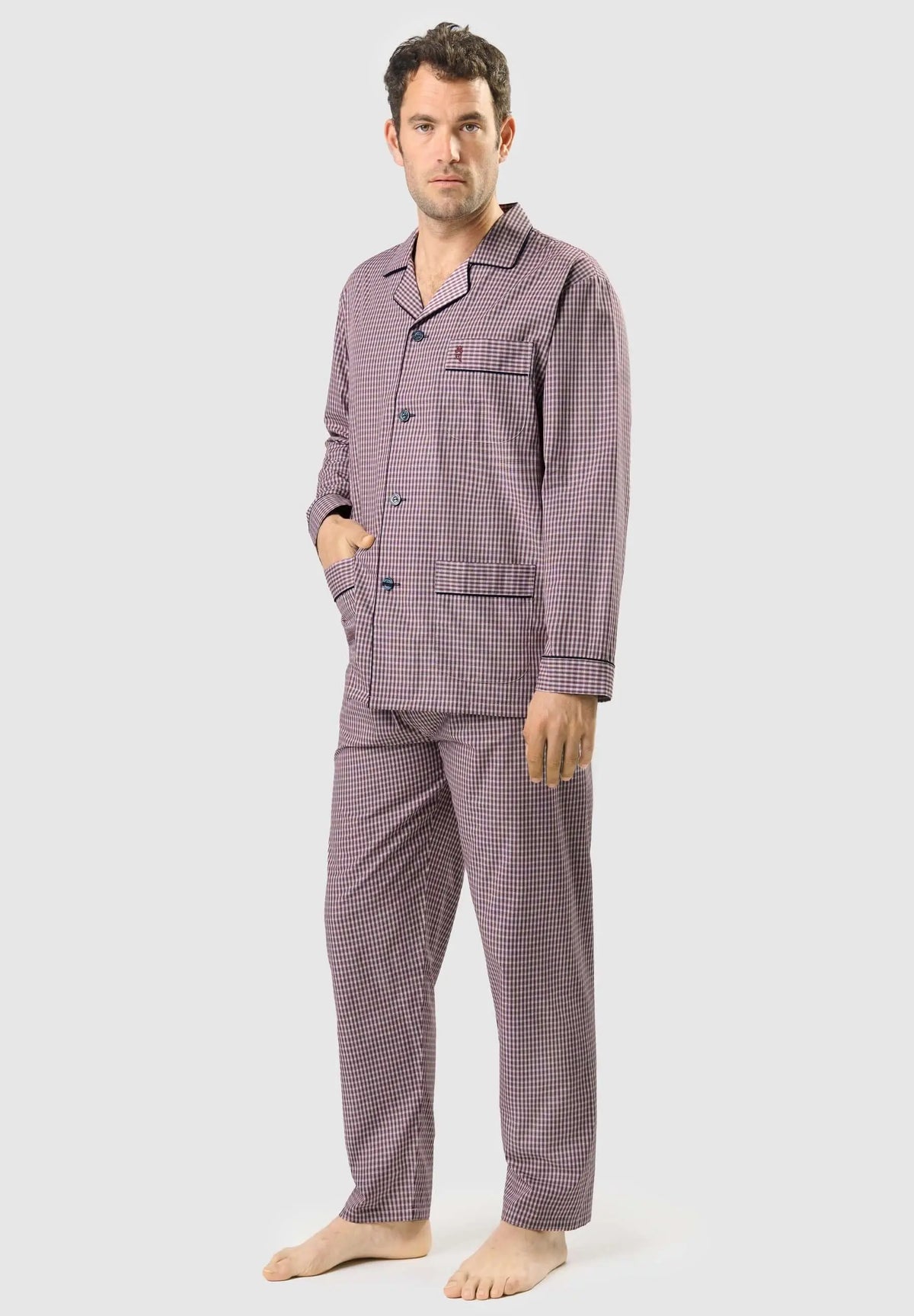 Hombre con pijama largo de cuadros rojos y negros, de solapa, botones y bolsillos, estilo clásico de popelín.