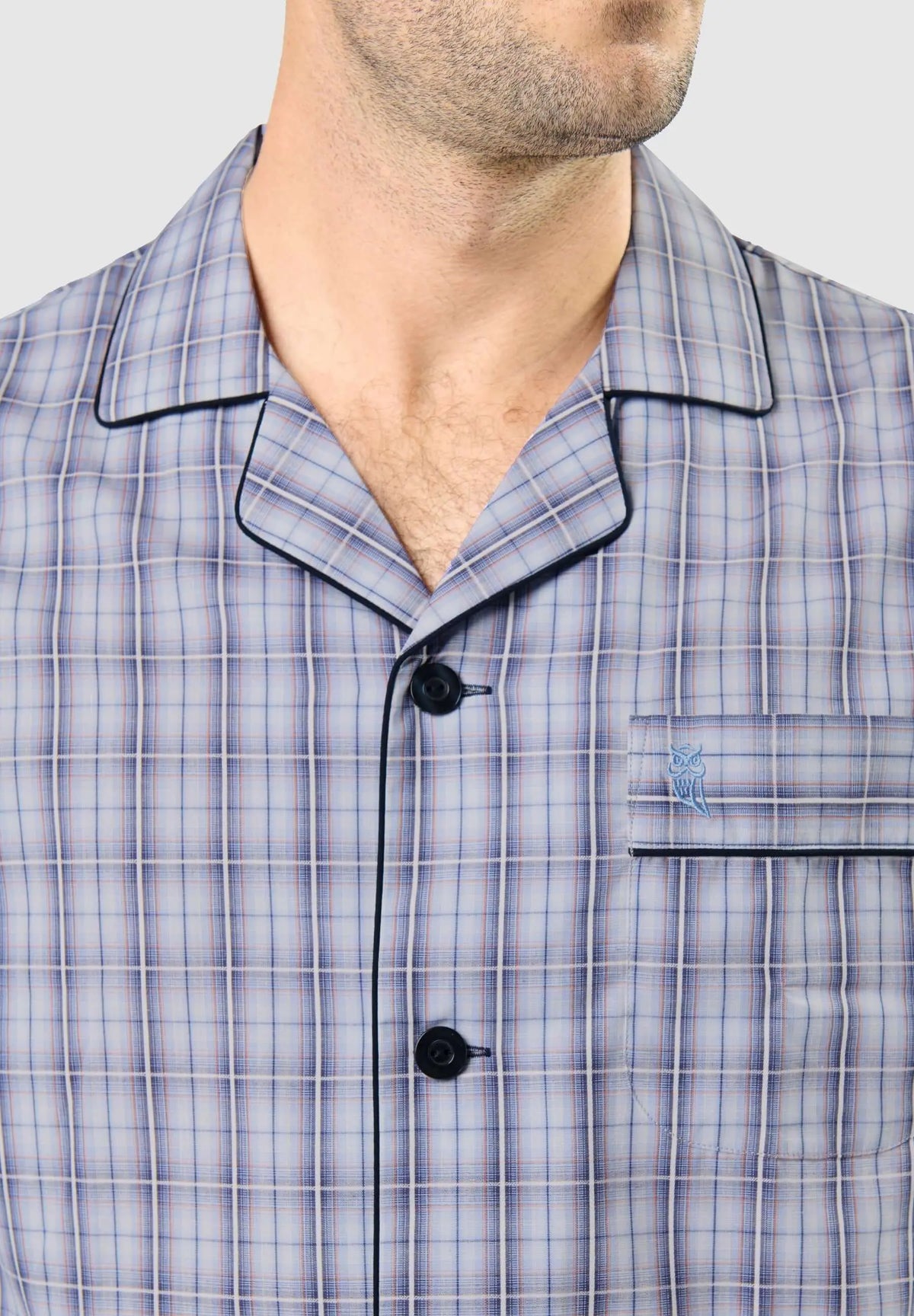 Pijama de hombre con cuello solapa, estampado de cuadros azul y blanco, botones oscuros, bolsillo y logo de búho bordado.
