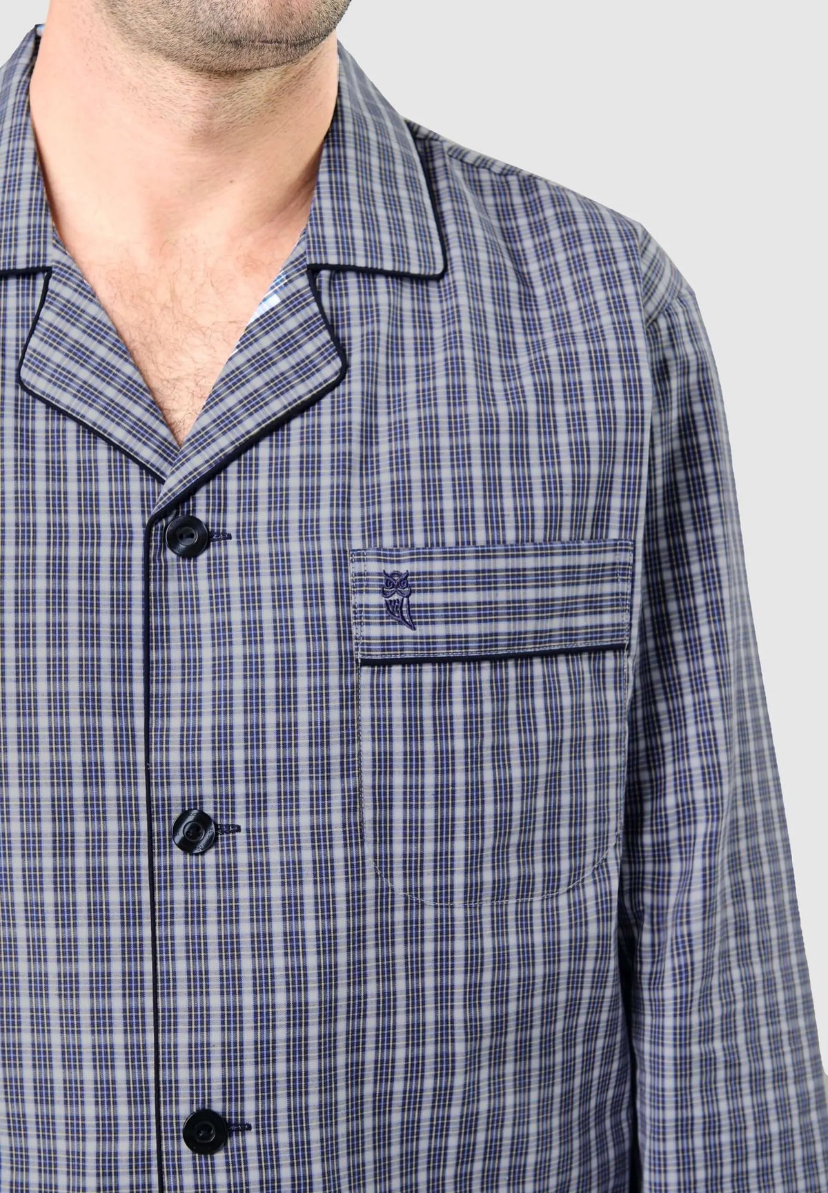 Pijama hombre de cuadros azul y gris, con solapas, botones oscuros, bolsillo frontal y logo de búho bordado.