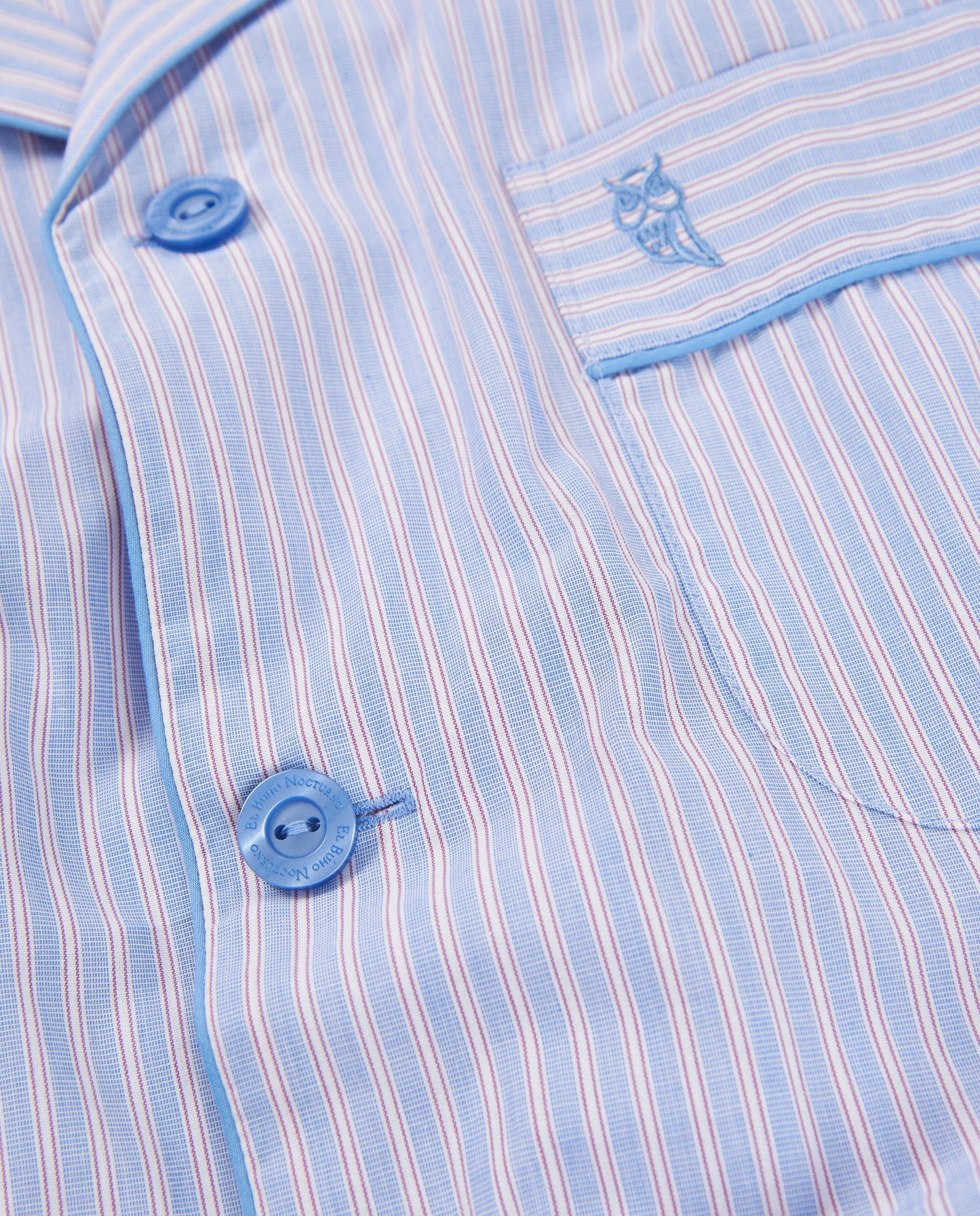 Camisa de pijama azul con rayas rosas y blancas, algodón suave, bolsillo con bordado de búho, botones azules.