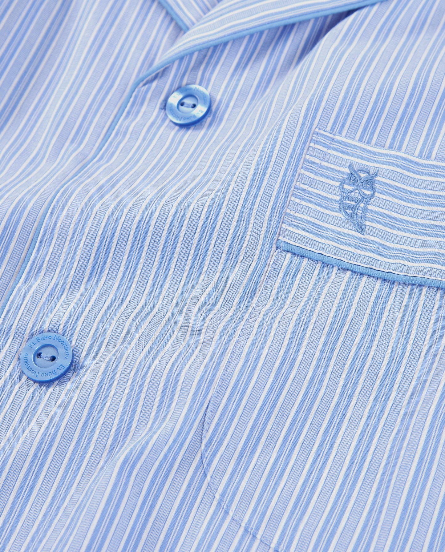 Camisa de pijama de rayas azul claro, algodón suave, con botones y bordado en el bolsillo. Ideal para descanso.