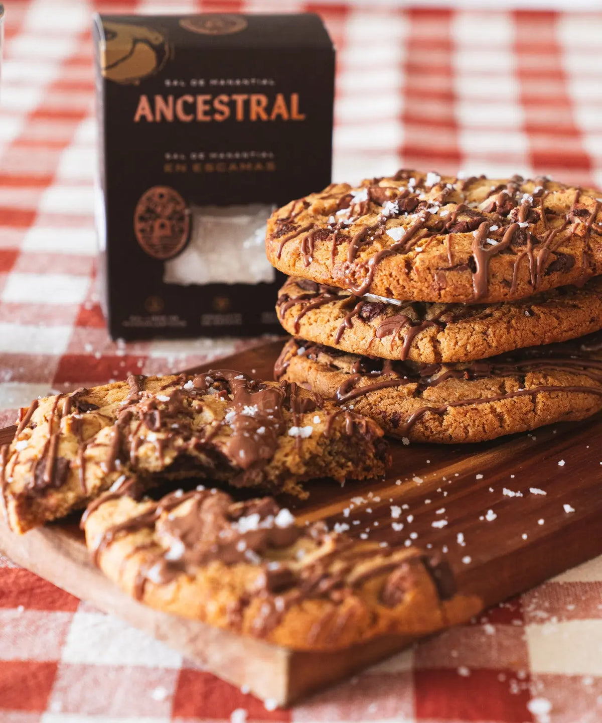 Stack of chocolate chip cookies drizzled with chocolate and sprinkled with natural spring salt flakes on a wood board.