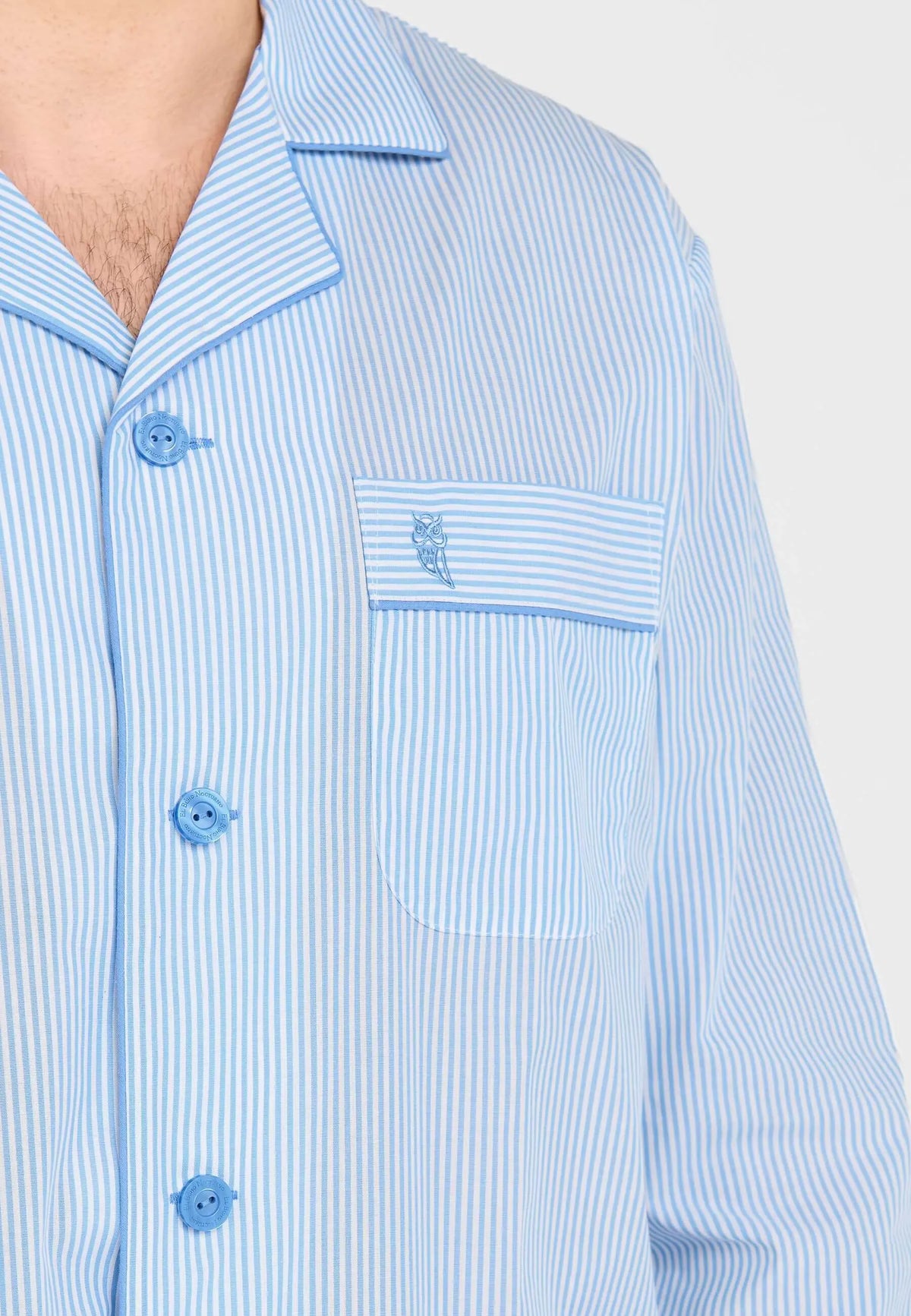 Pijama hombre de solapa, tejido popelín a rayas azul y blanco, bolsillo con bordado de búho y botones azules.