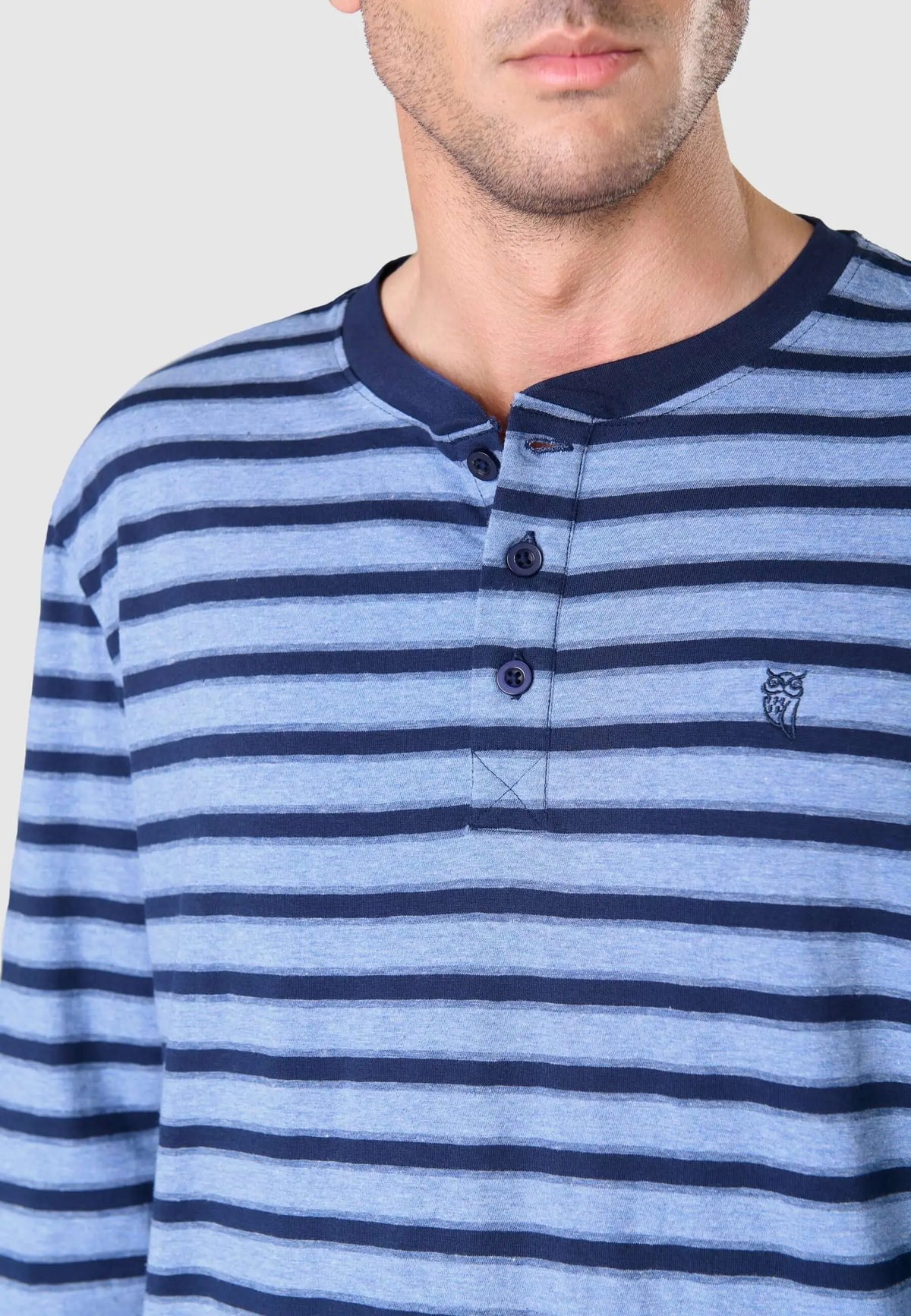 Pijama hombre de punto a rayas azules con cuello redondo, tapeta de tres botones y logo de búho bordado.