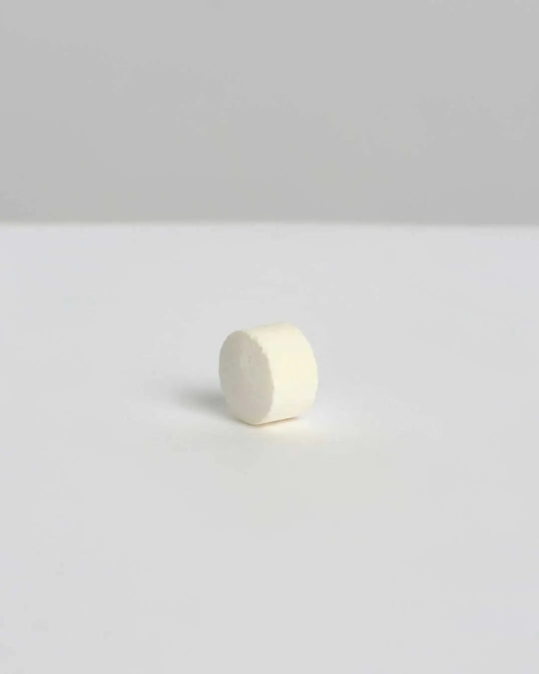 Pastilla de pasta de dientes blanca de Banbu, de textura compacta y forma cilíndrica, sobre fondo neutro minimalista.