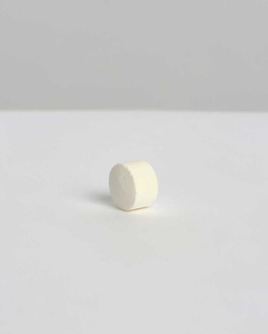 Pastilla de pasta de dientes blanca de Banbu, de textura compacta y forma cilíndrica, sobre fondo neutro minimalista.