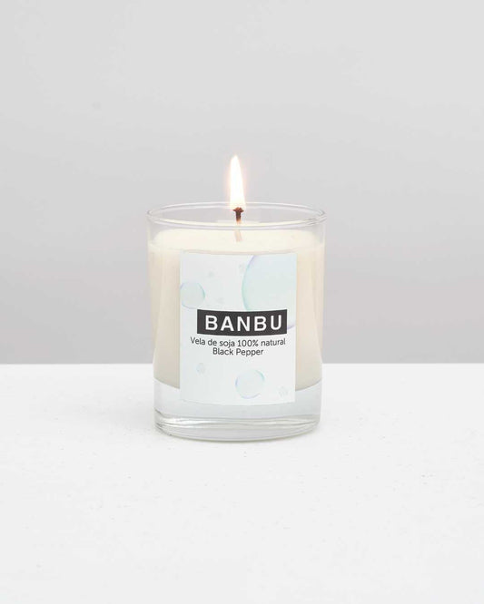 Vela de soja natural BANBU Black Pepper encendida en vaso de vidrio sobre superficie blanca. Diseño minimalista.