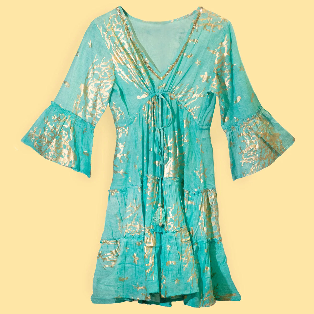 Vestido corto turquesa de corte fluido con estampado dorado, escote en V, mangas acampanadas y detalle de borlas.