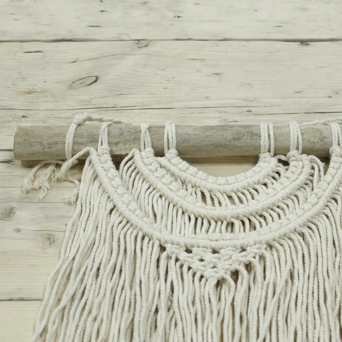 Tapiz de macramé beige con detalles en madera, estilo bohemio, perfecto para decoración de pared.