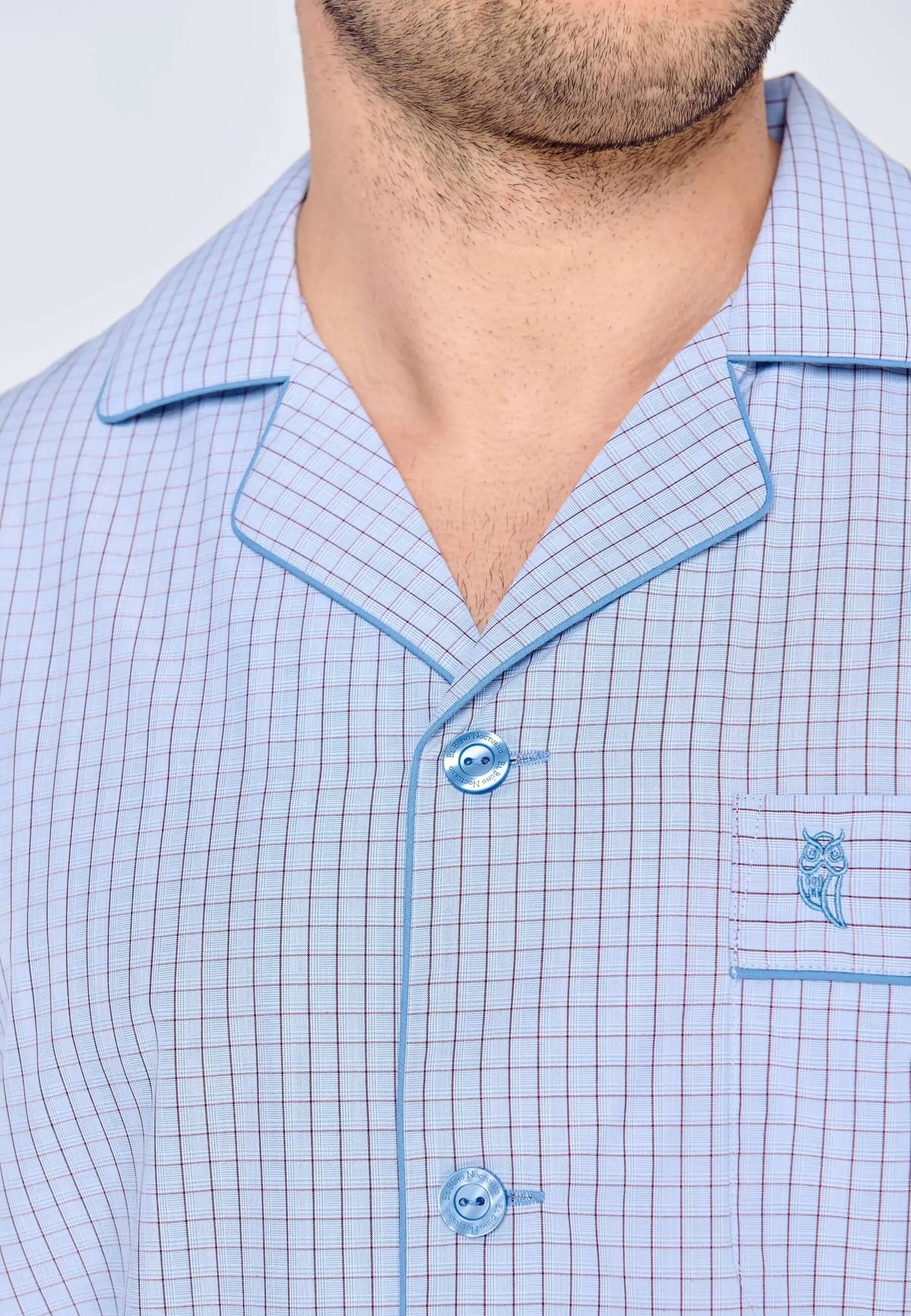 Pijama de hombre azul con cuadros, cuello solapa, botones a juego, ribete azul y logo de búho bordado en el bolsillo.