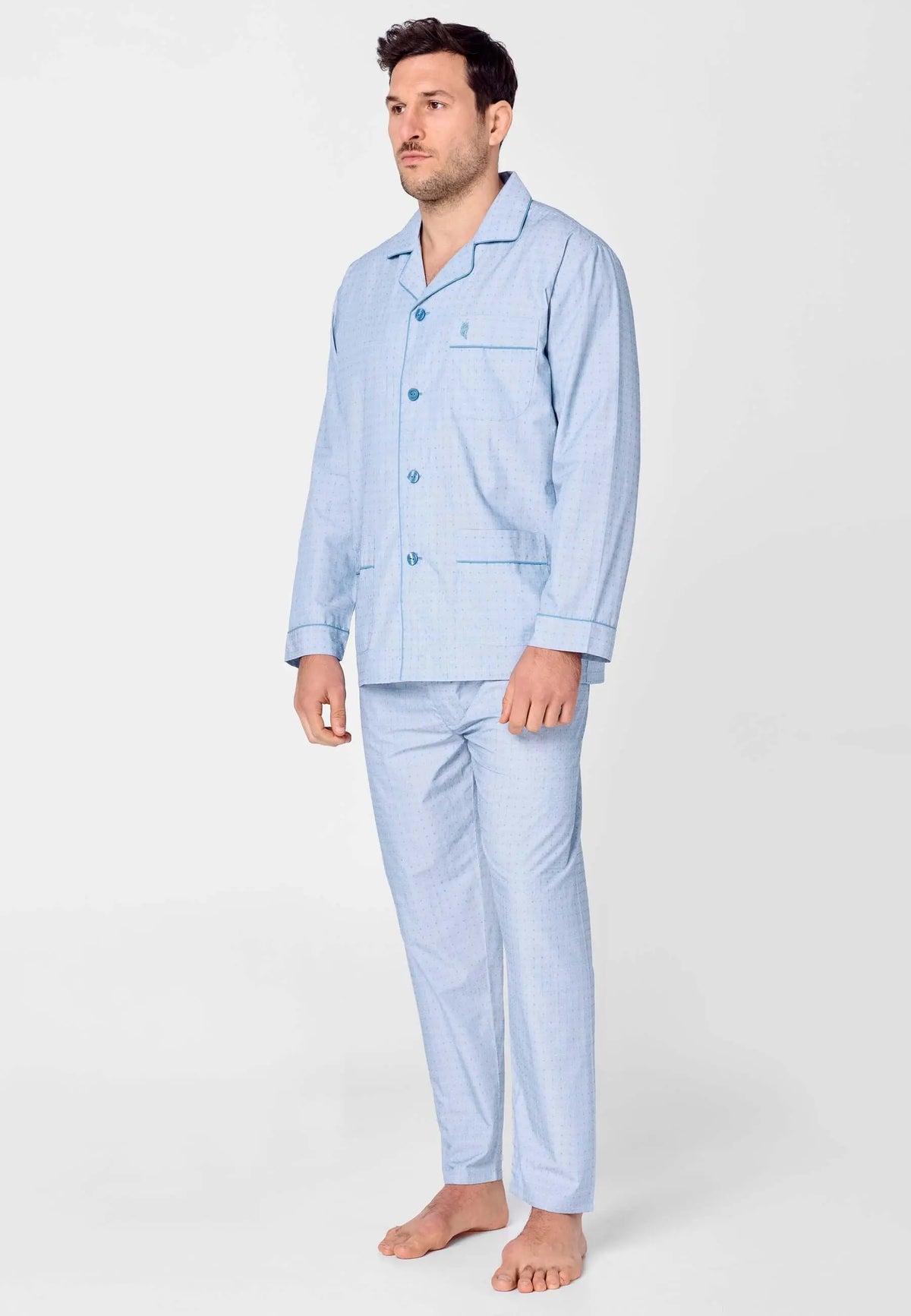 Pijama de hombre azul con estampado geométrico, chaqueta de solapa con botones y pantalón largo, puesto por un modelo.