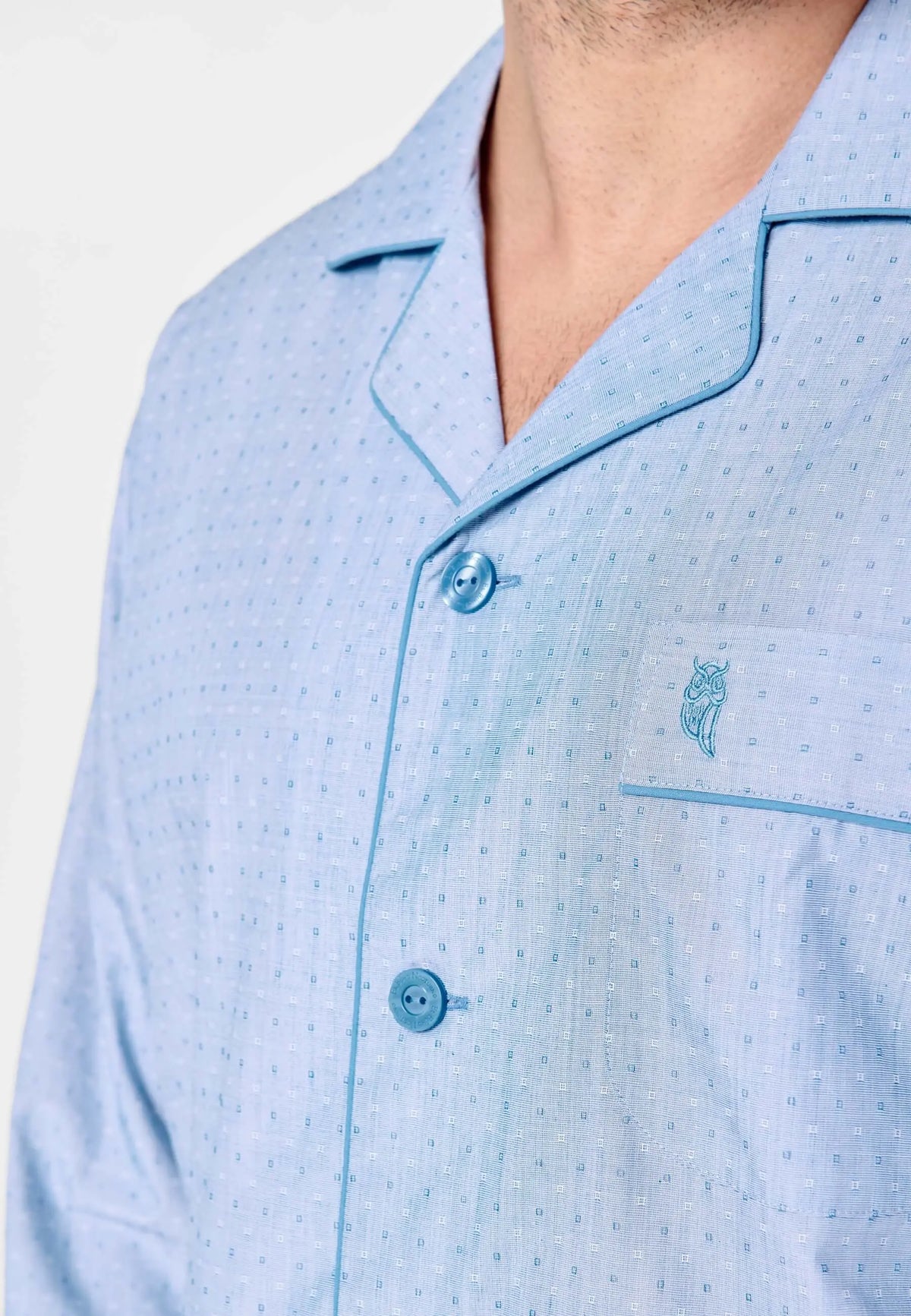 Pijama azul claro de hombre con solapas, botones, bolsillo frontal y estampado geométrico pequeño con logo de búho.