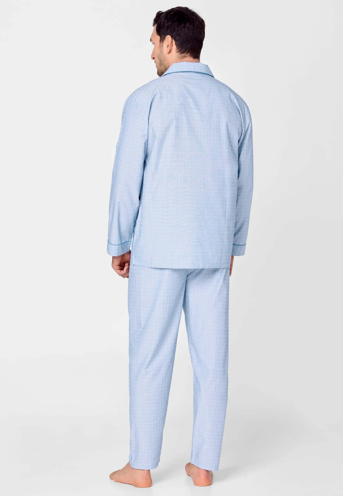 Hombre de espaldas con pijama azul de manga larga, cuello solapa y estampado de pequeños puntos sobre fondo claro.