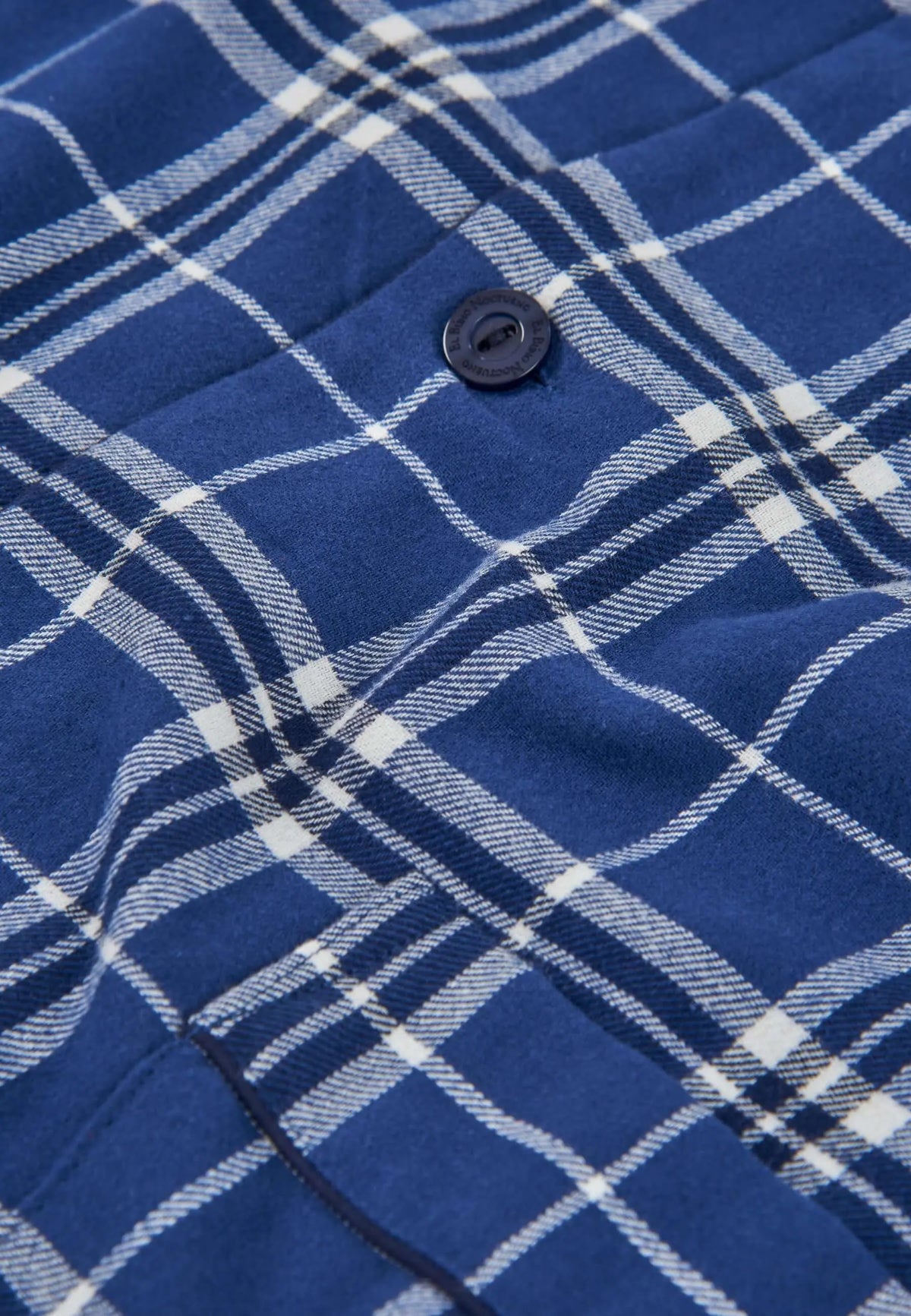 Detalle de pijama de franela azul con estampado de cuadros blancos y botón oscuro grabado de la marca El Búho Nocturno.