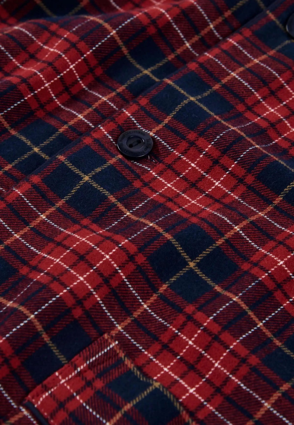 Detalle de tejido franela a cuadros rojos y azul marino con botón negro de pijama de hombre El Búho Nocturno.