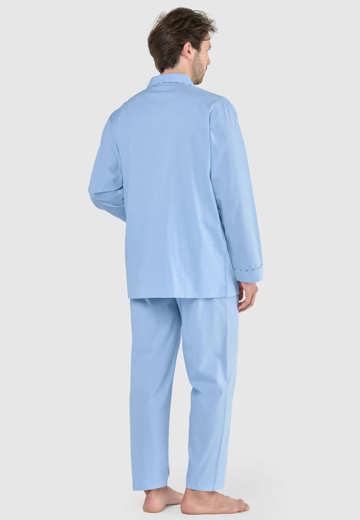 Pijama largo de hombre azul celeste liso. Hombre de espaldas con chaqueta de solapa y pantalón a juego, tejido mate.